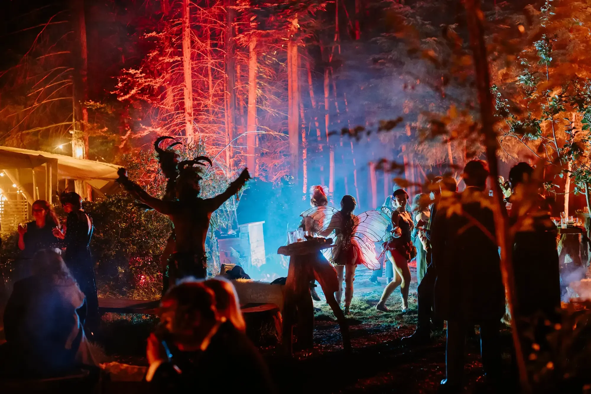 Costumed guests dancing in an illuminated forest at a nighttime immersive event