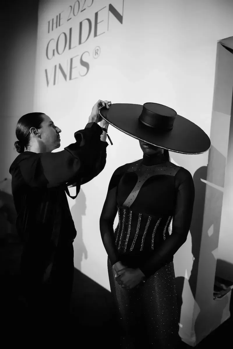 Performer in an embellished dress having a hat adjusted at the Golden Vines Awards
