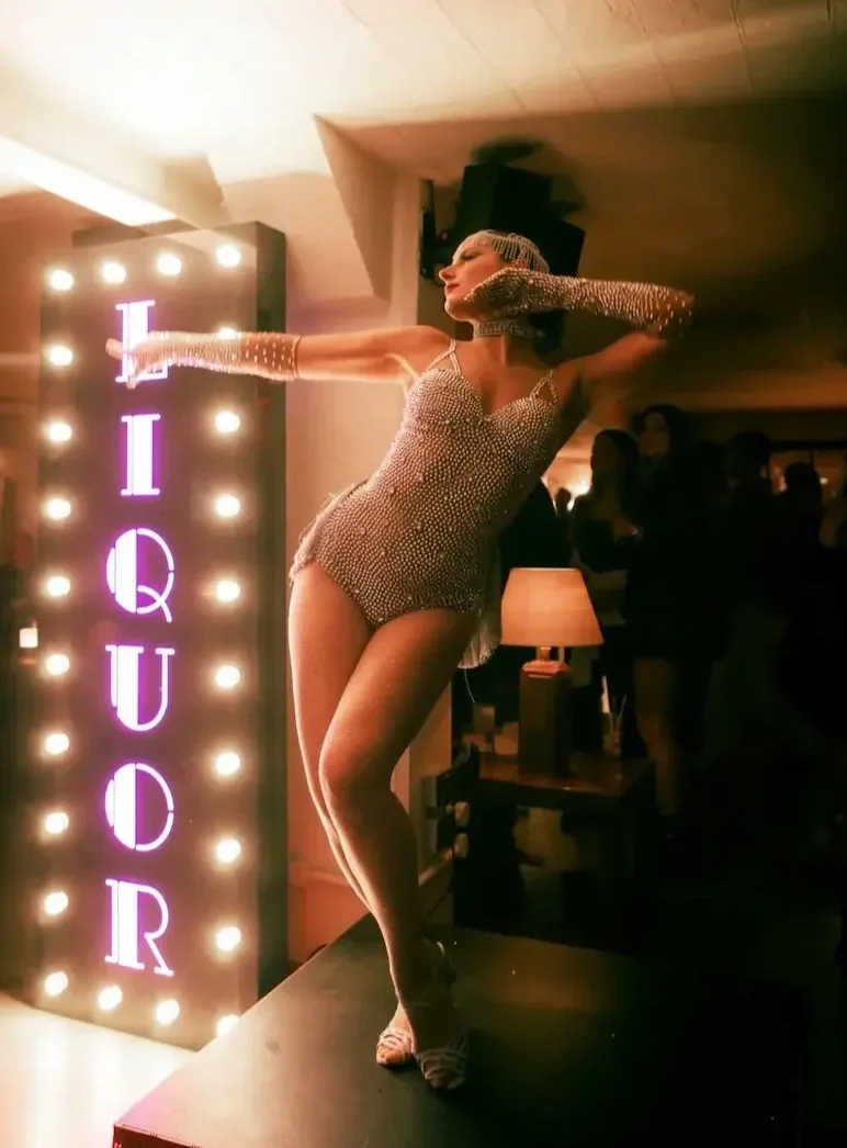 Performer in a rhinestone costume posing before vintage liquor signage at exclusive party