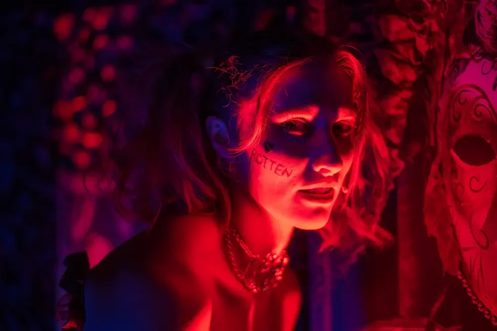 Performer with artistic face paint illuminated by neon lighting at themed event