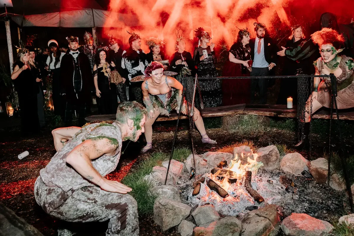 Fantasy-costumed performers around a campfire with red smoke and dramatic lighting during an immersive experience