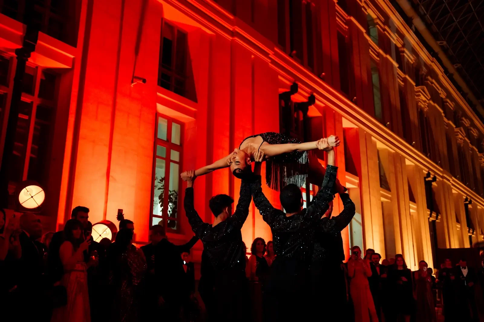 Acrobatic performance with dancer lifted at red-lit venue at a red carpet gala