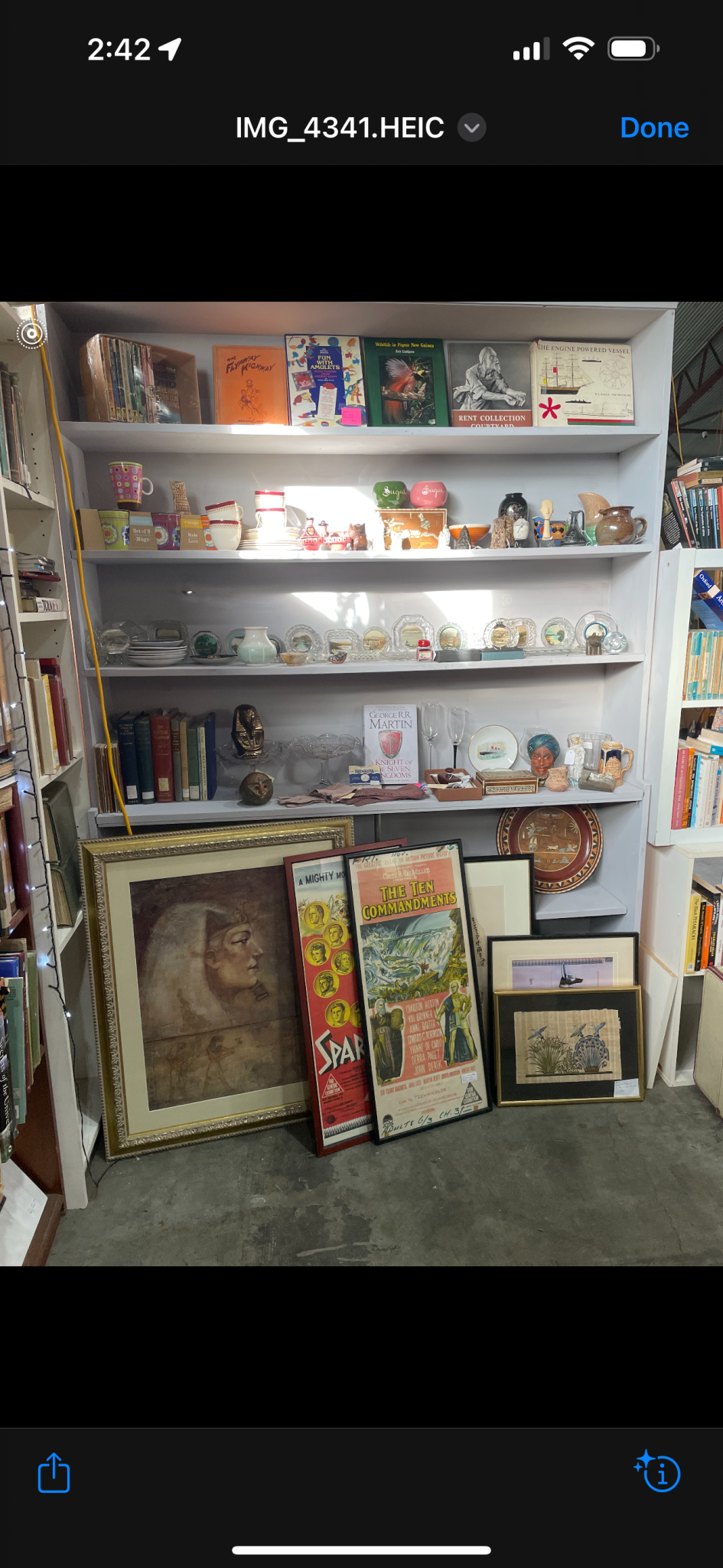 Bookshelf with various books, ceramics, glassware, and framed posters at Waverley Antique Bazaar Stall H20.