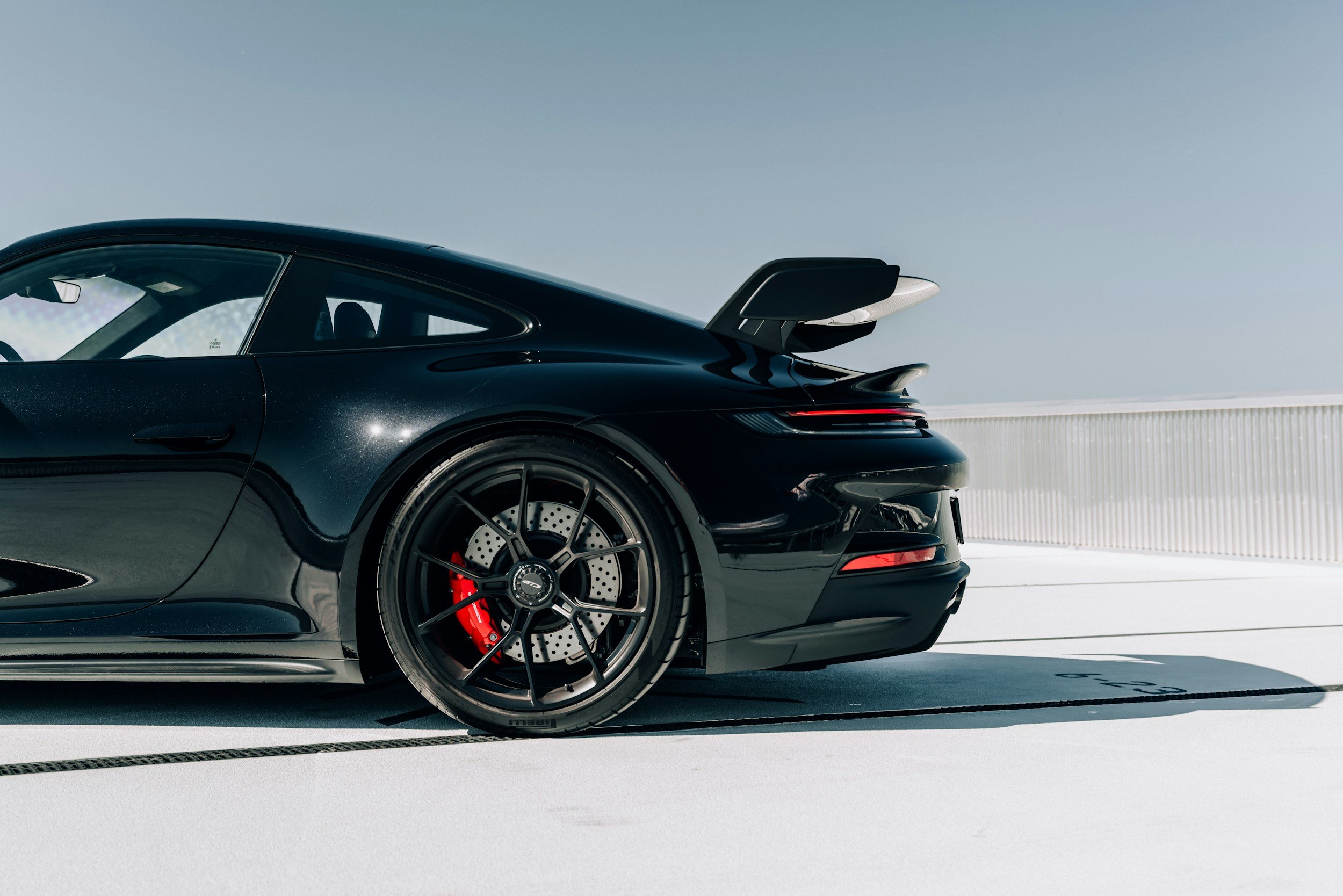 Porsche 911 GT3 auf einer weißen Teststrecke bei sonnigem Himmel, Spurmarkierungen sichtbar.