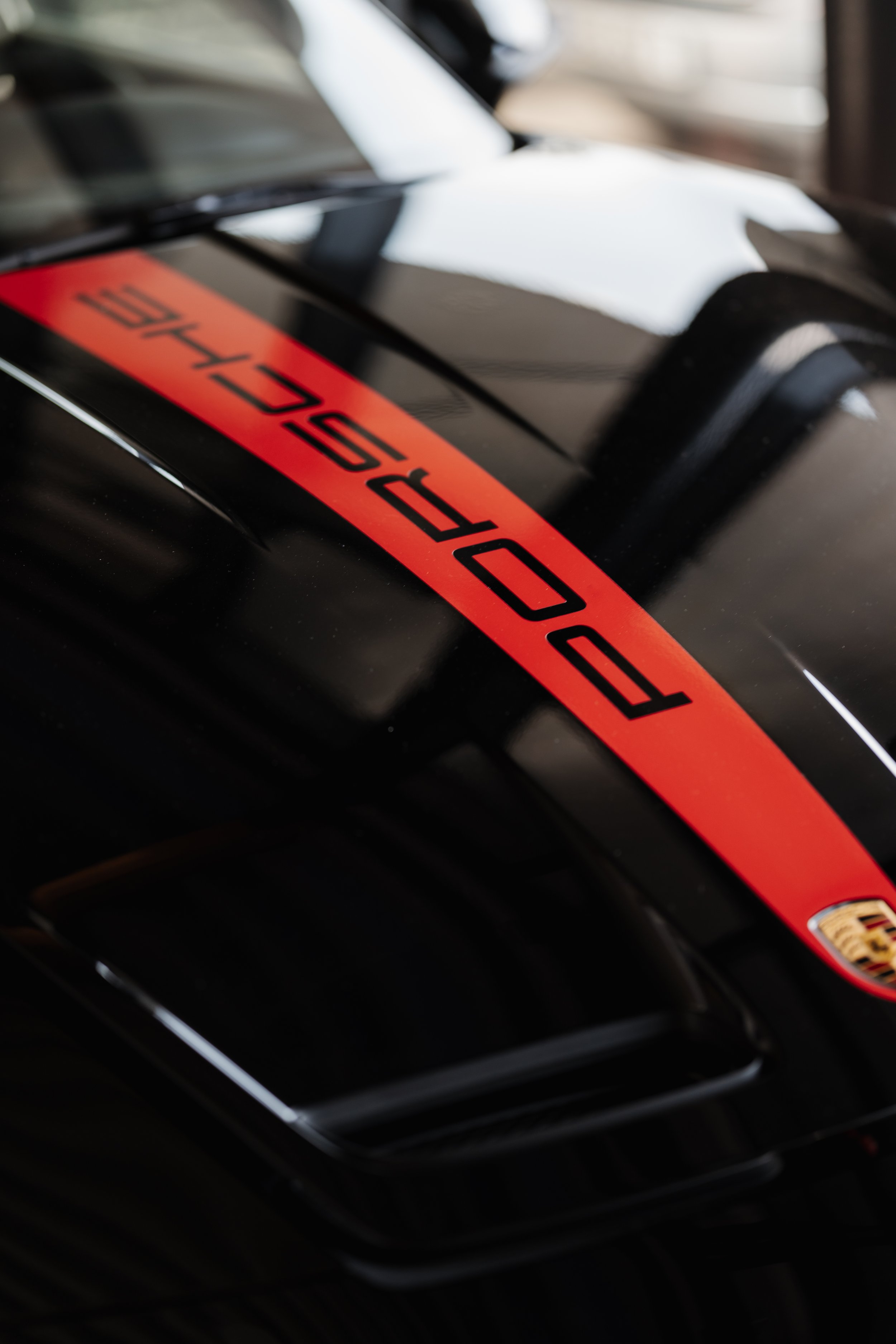 Das Porsche-Logo auf einem schwarzen Auto, mit einer reflektierenden sturmverhangenen Stadtlandschaft im Hintergrund.