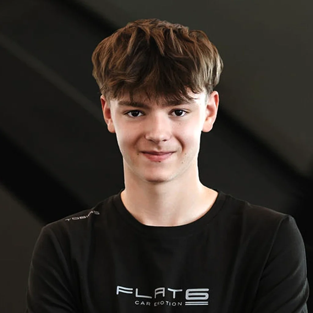 Junge trägt schwarzes T-Shirt mit weißem Logo, lächelt, kurz braune Haare, dunkler Hintergrund.