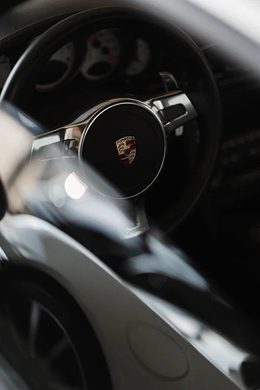 Innenraum eines Porsche-Fahrzeugs, Fokus auf das Lenkrad mit Porsche-Logo in der Mitte.