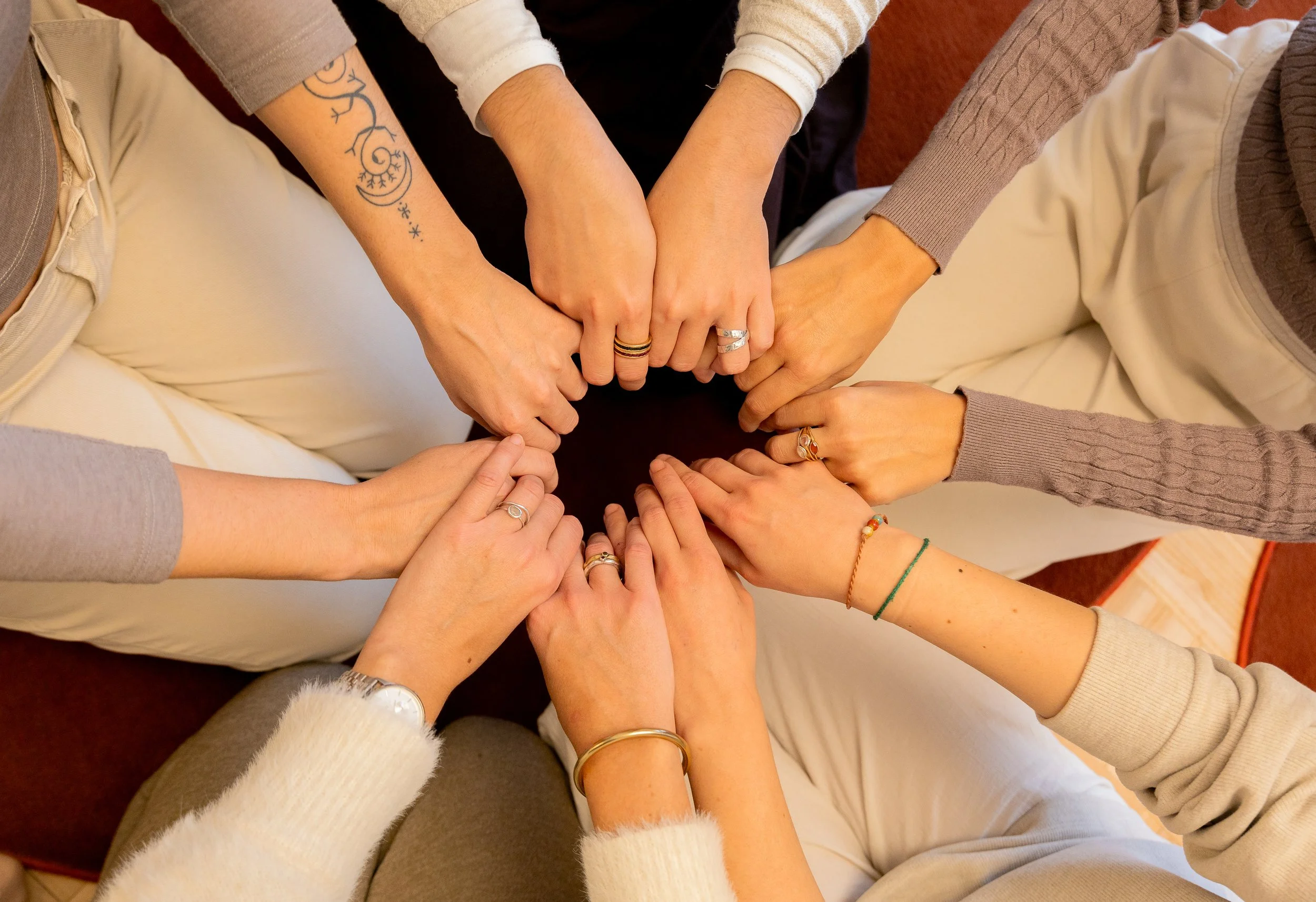 Siete manos unidas formando un círculo, mostrando diversidad en accesorios y tatuajes.