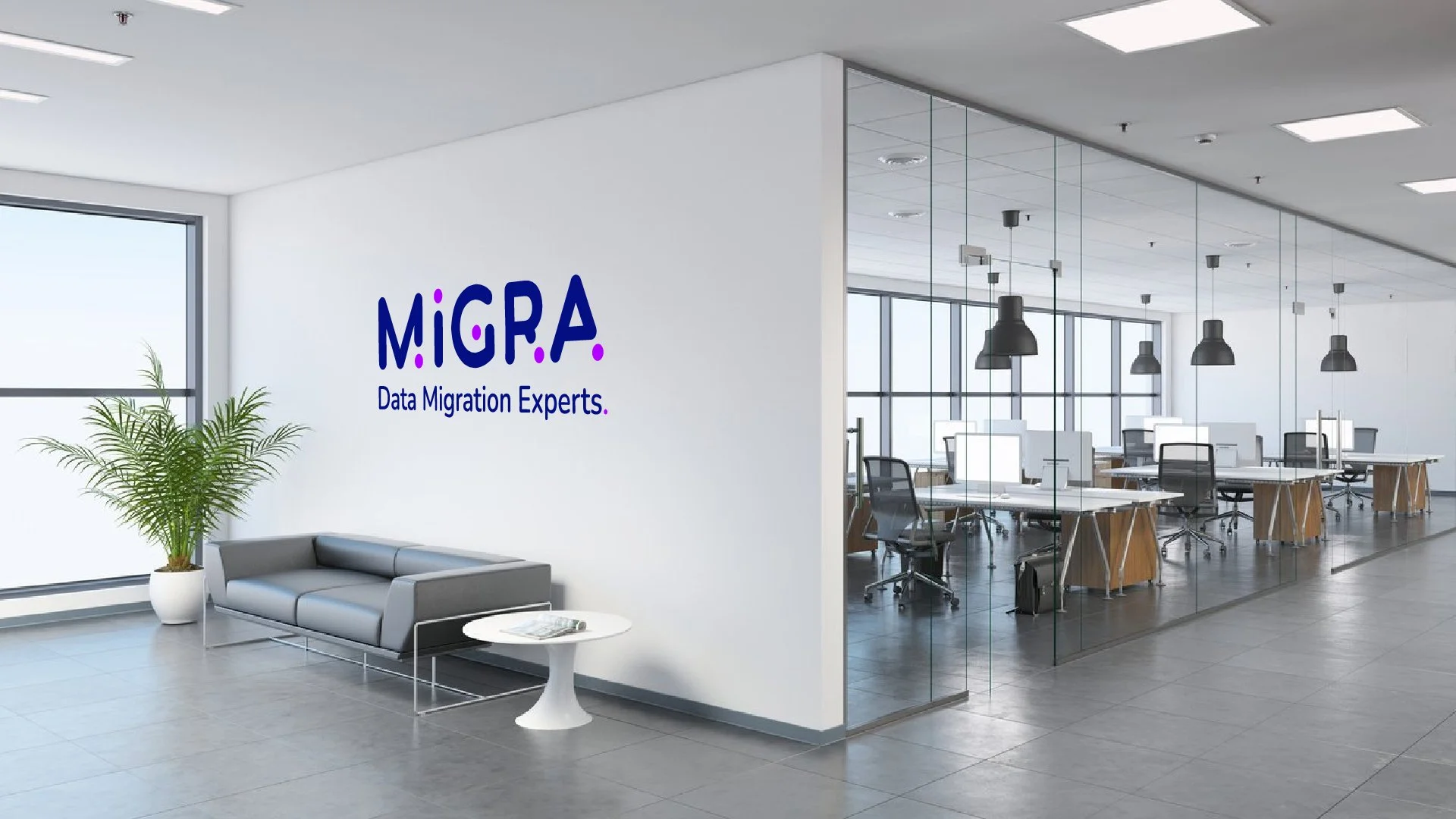 Modern office lobby with a gray sofa and a white side table next to a large window and a potted plant. A glass-walled conference room with desks and chairs is visible in the background. The company's logo, 'MiGRA Data Migration Experts,' is on the white wall.