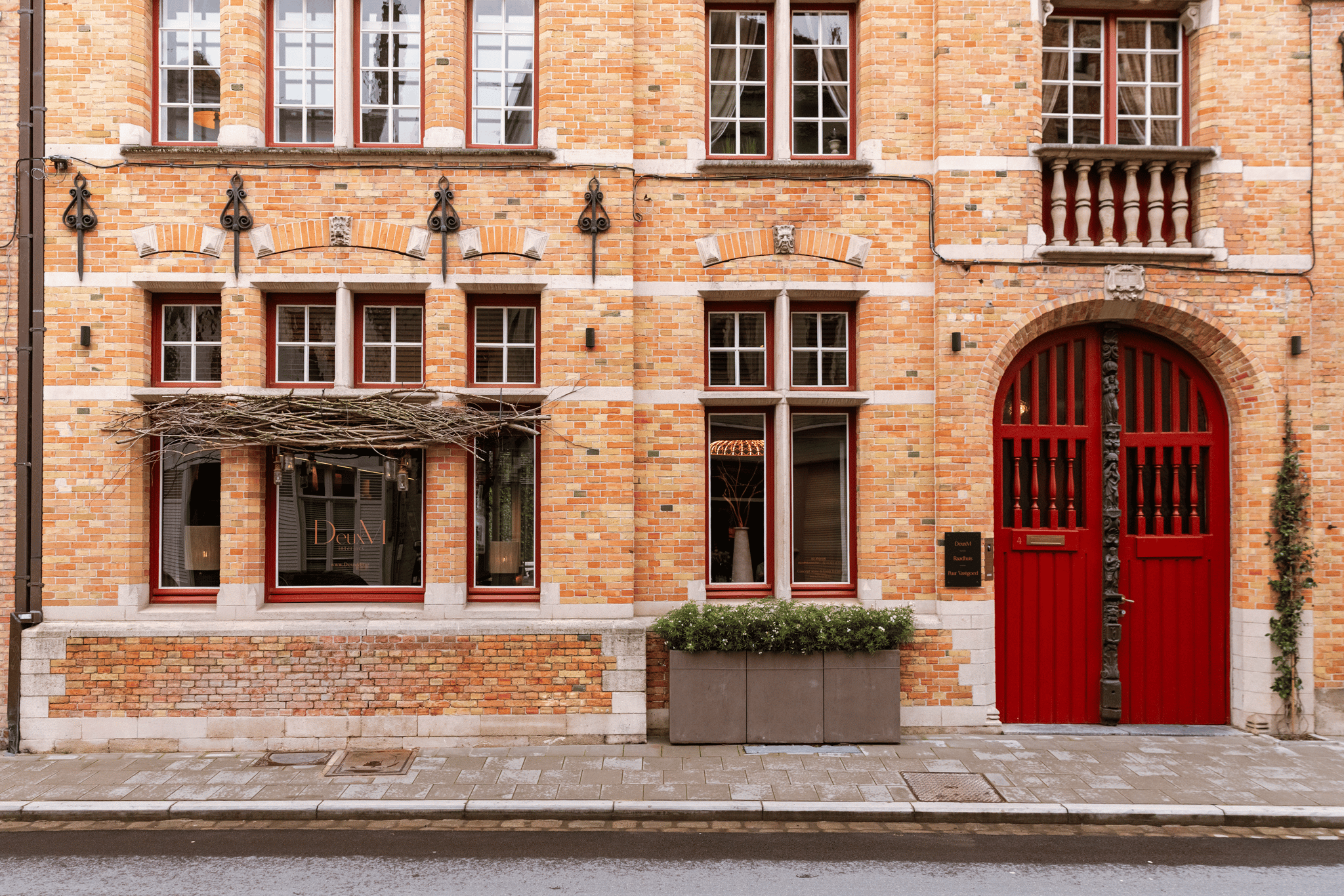 A brick building facade with multiple windows, a decorative arch doorway with red doors, and ornate metal details above the windows.