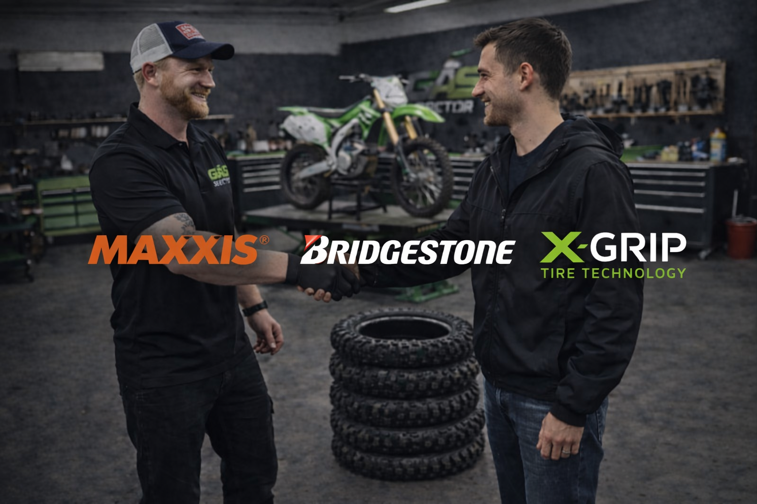 Two men shaking hands in a garage with a dirt bike on a lift in the background and tires to the side. The man on the left is wearing a black shirt and a cap, while the man on the right is wearing a black hoodie. Logos for MAXXIS, BRIDGESTONE, and X-GRIP Tire Technology are overlaid on the image.
