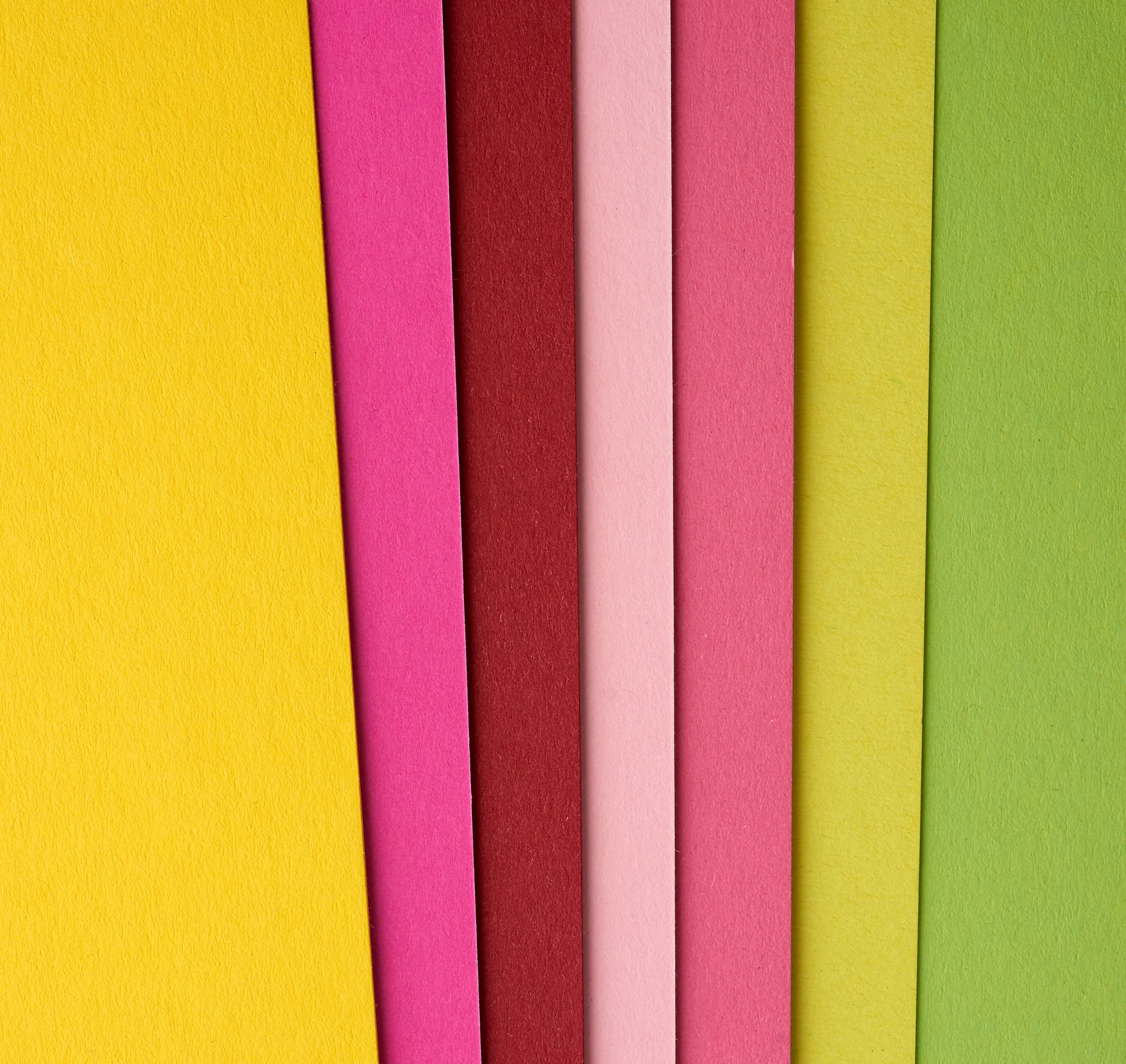 Kleurige vellen papier in geel, roze, rood, lichtroze, donkerroze, geelgroen en groen, verticaal gerangschikt.