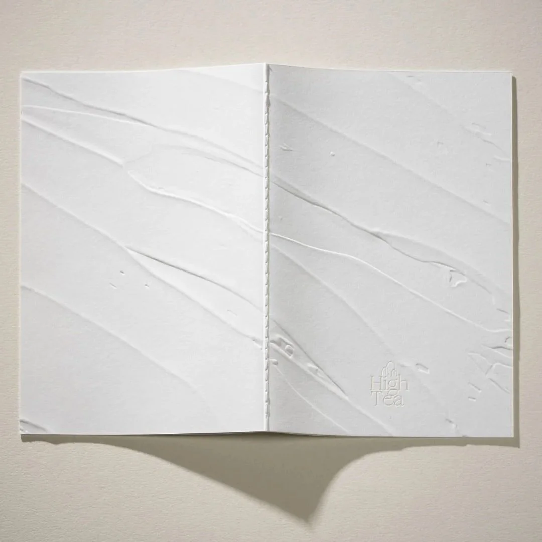 Open menu cover with  a textured surface, and an embossed logo that reads 'High Tea'.