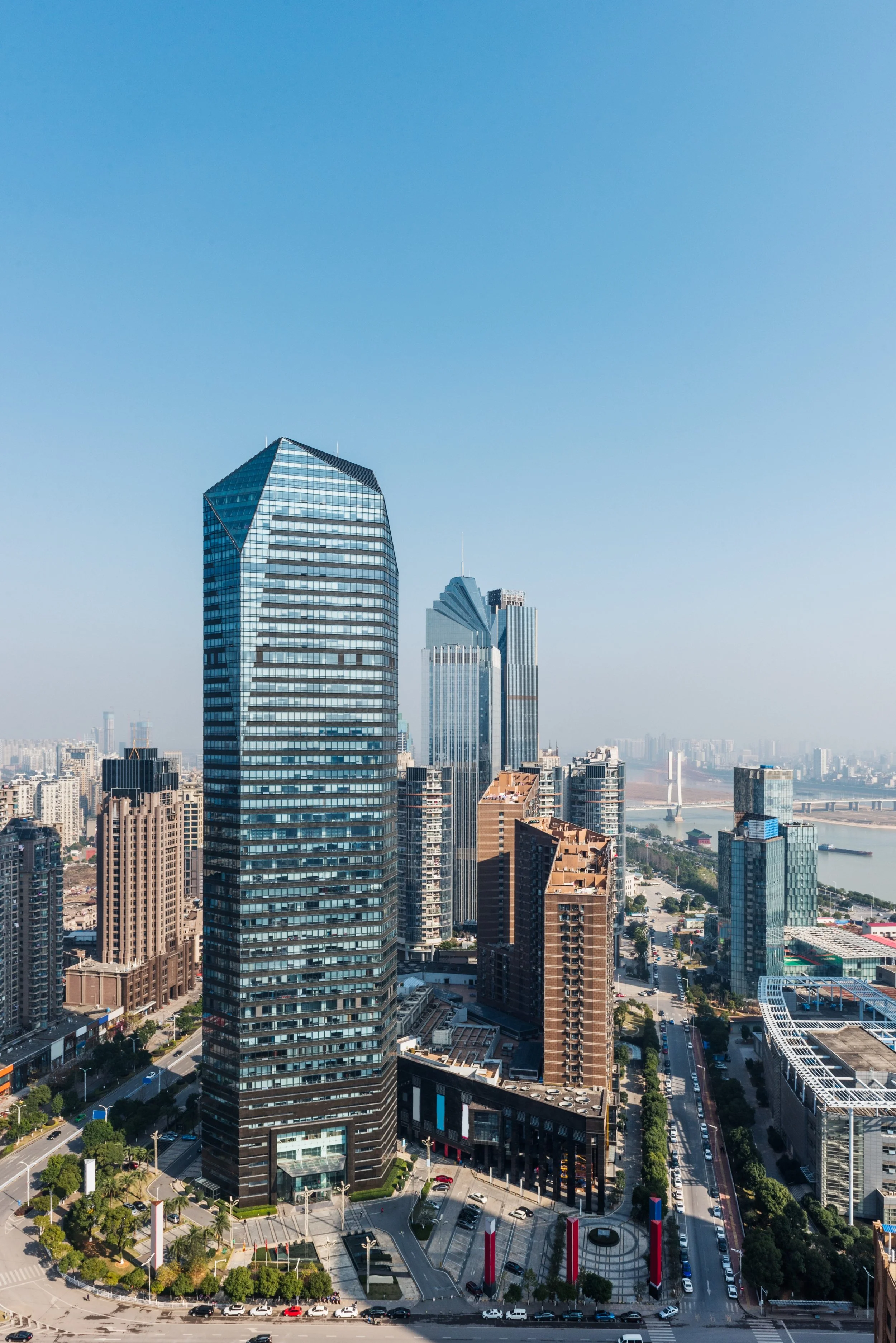 View of a city skyline with modern skyscrapers, including a tall glass building, and a river in the background under a clear blue sky.