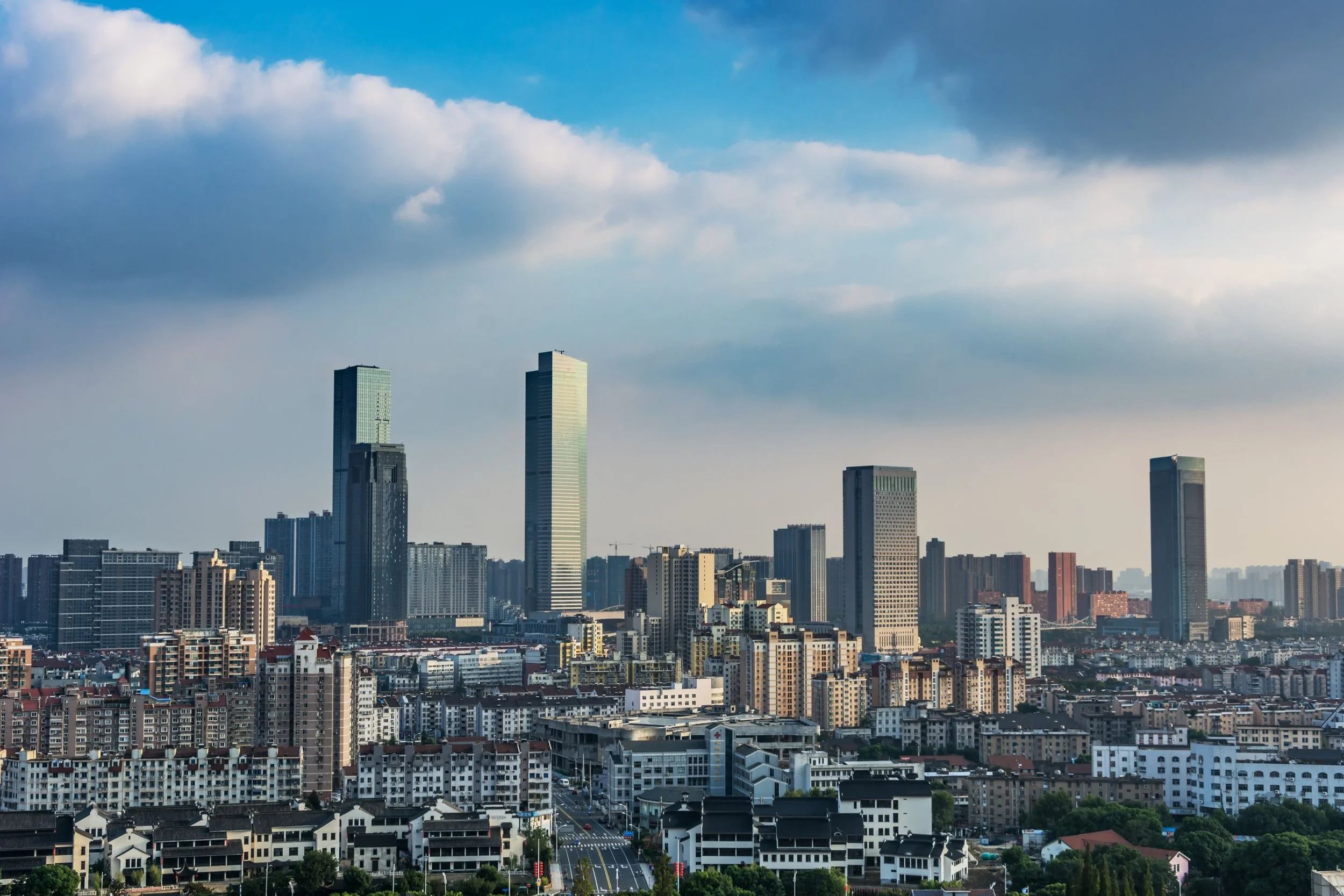 Skyline of a modern city with tall skyscrapers and numerous mid-rise buildings, under a partly cloudy sky.