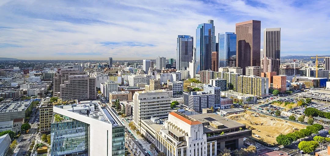 A cityscape featuring numerous high-rise buildings, with modern skyscrapers in the downtown area, under a partially cloudy sky.