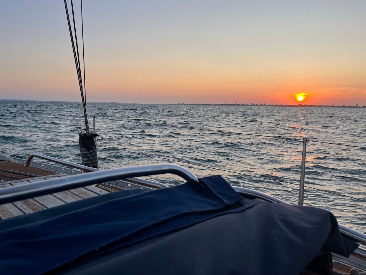 View from a sailing yacht towards an orange sunset and distant shoreline