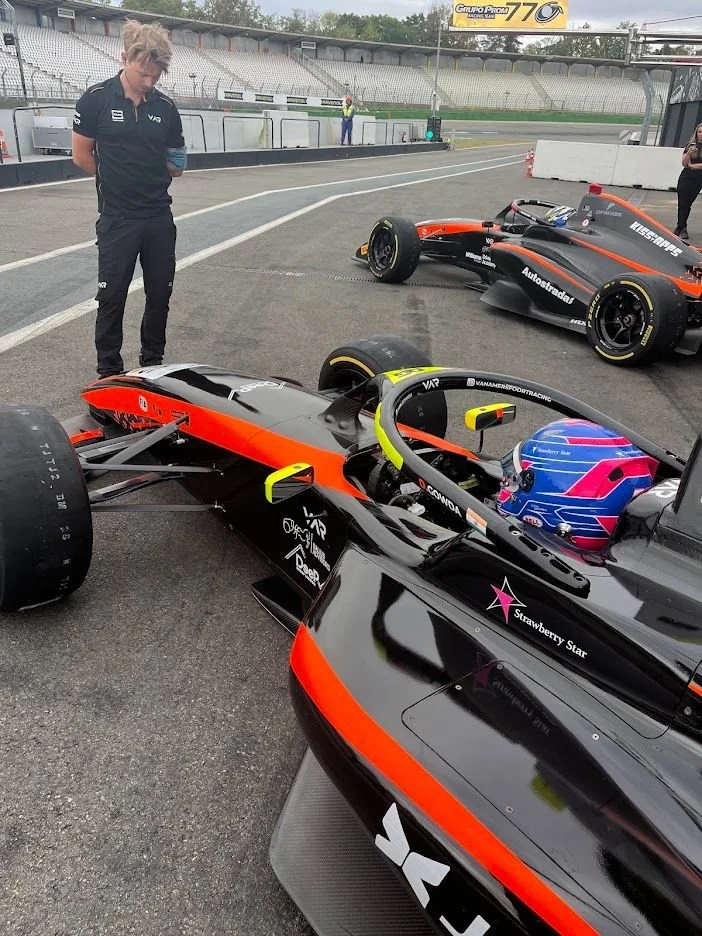 A racing driver in a single-seater car with a team member on the starting grid