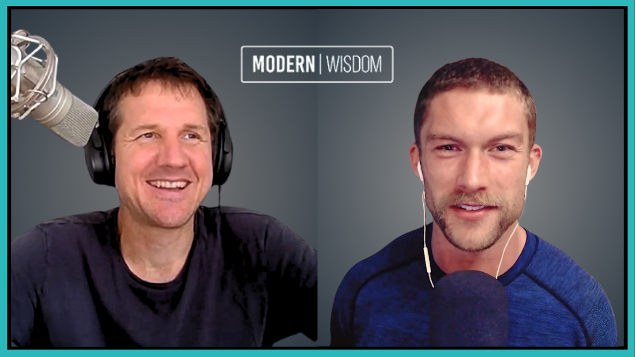 Two men engaged in a podcast recording, with one wearing headphones and speaking into a microphone, and the other wearing earphones, both smiling. The background features a sign that reads 'MODERN WISDOM'.