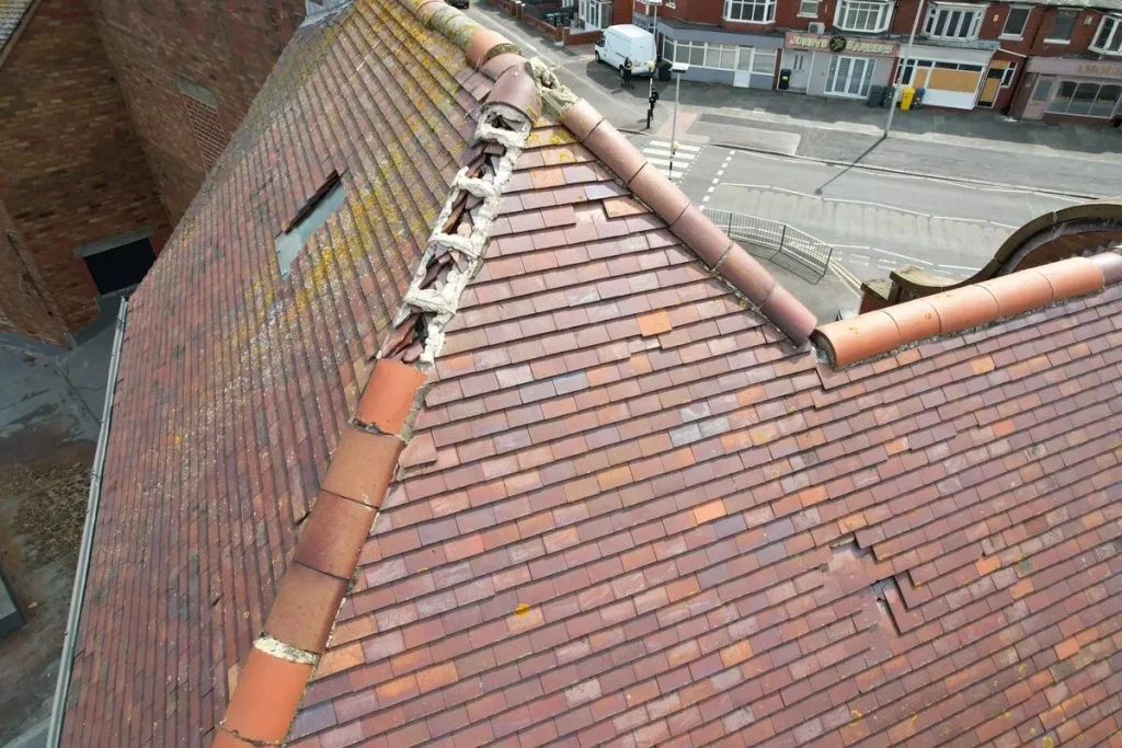 A damaged sloped tile roof with broken and missing tiles at the ridge, exposing the underlying structure.