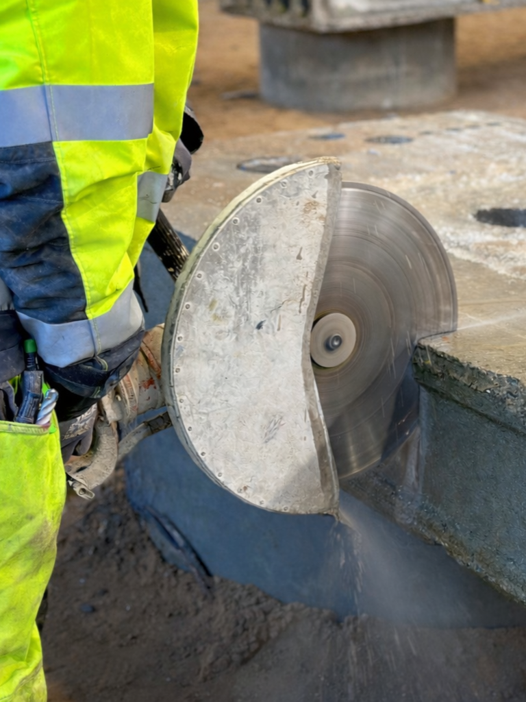 En person i refleksvest bruger en rundsav til skæring i beton.