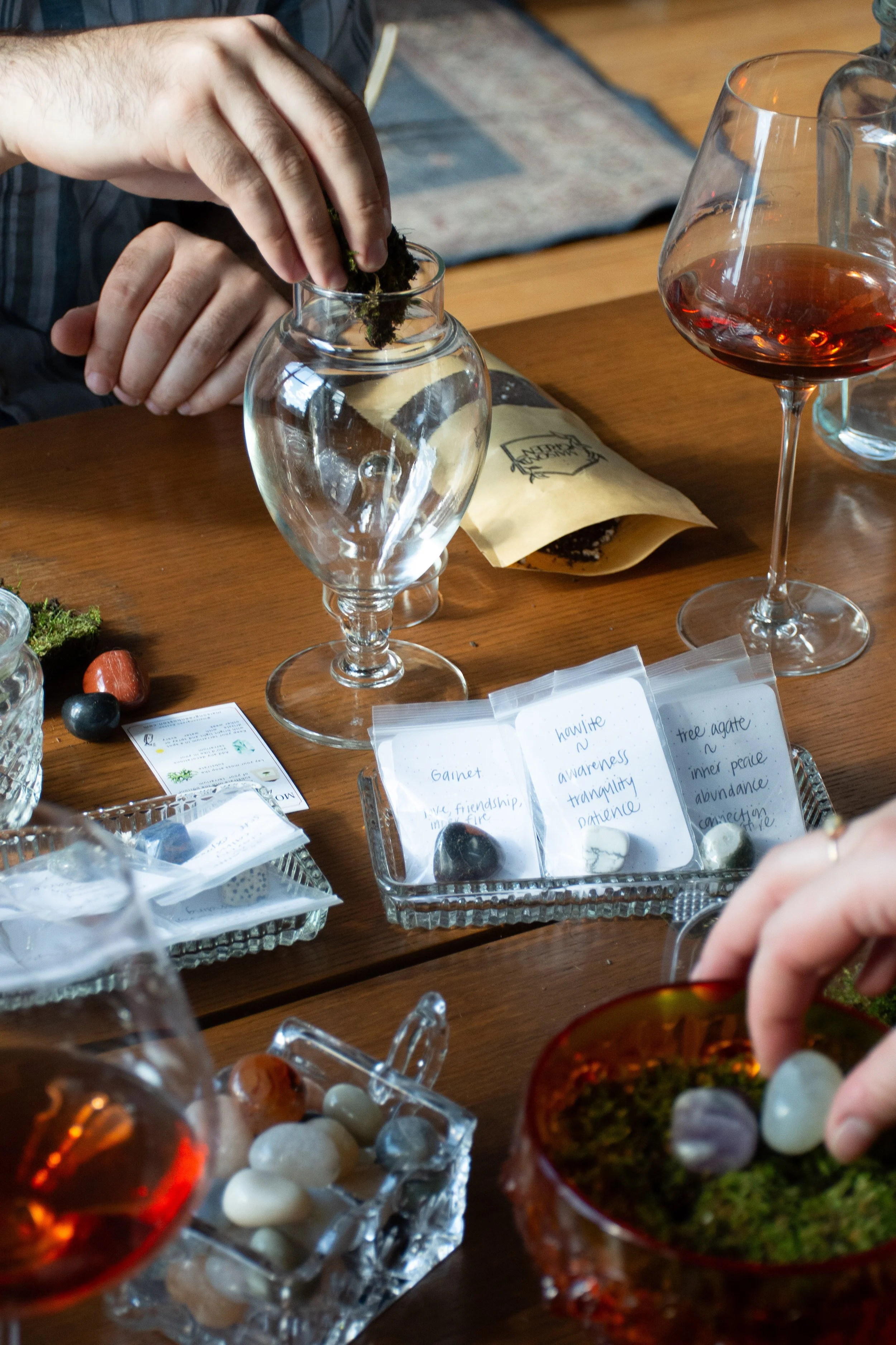 People preparing for a tarot card reading, with various crystals, notes, and glasses of wine on the table.