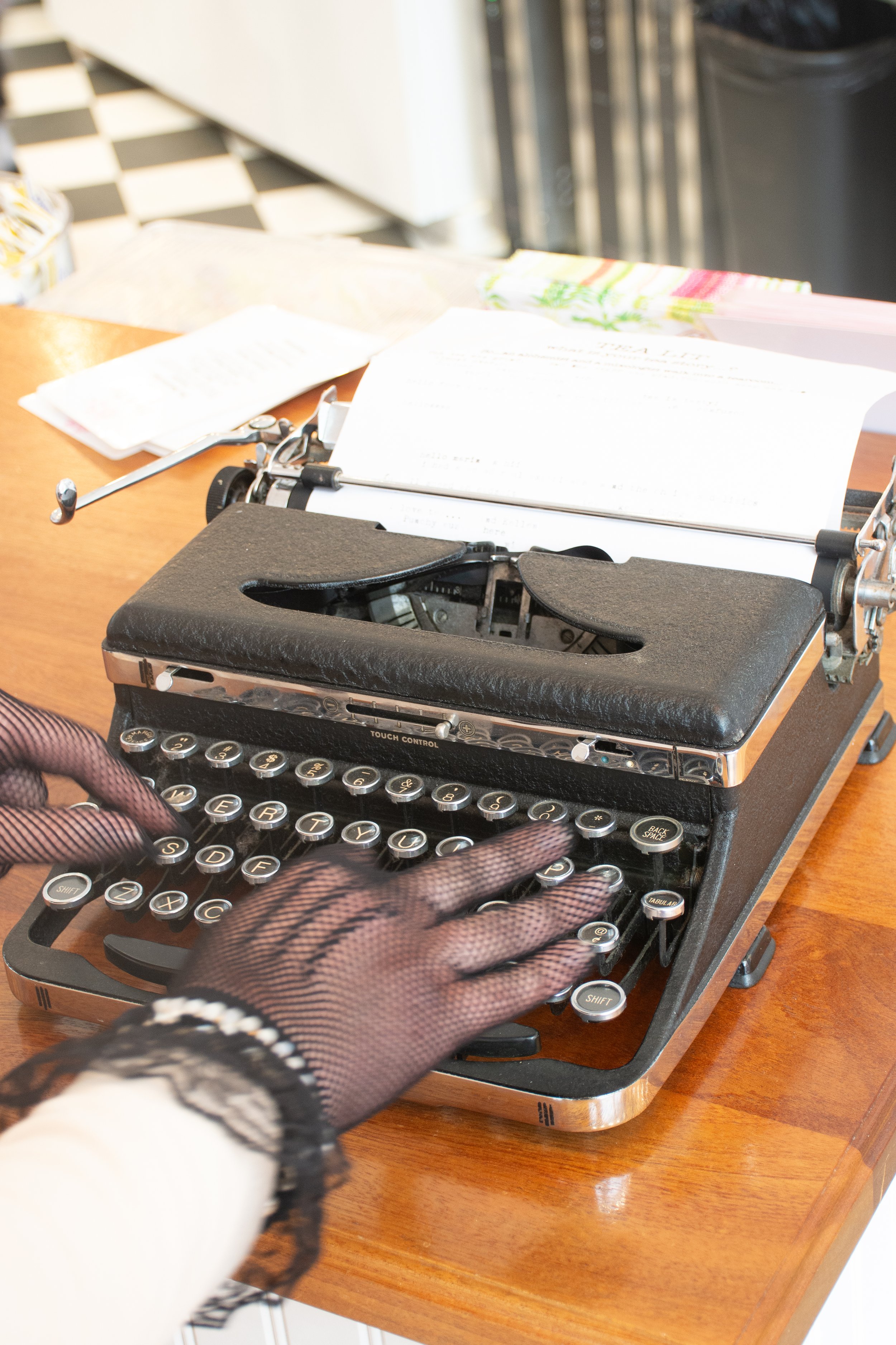 A person's hands typing on a vintage typewriter with paper loaded, placed on a wooden table.