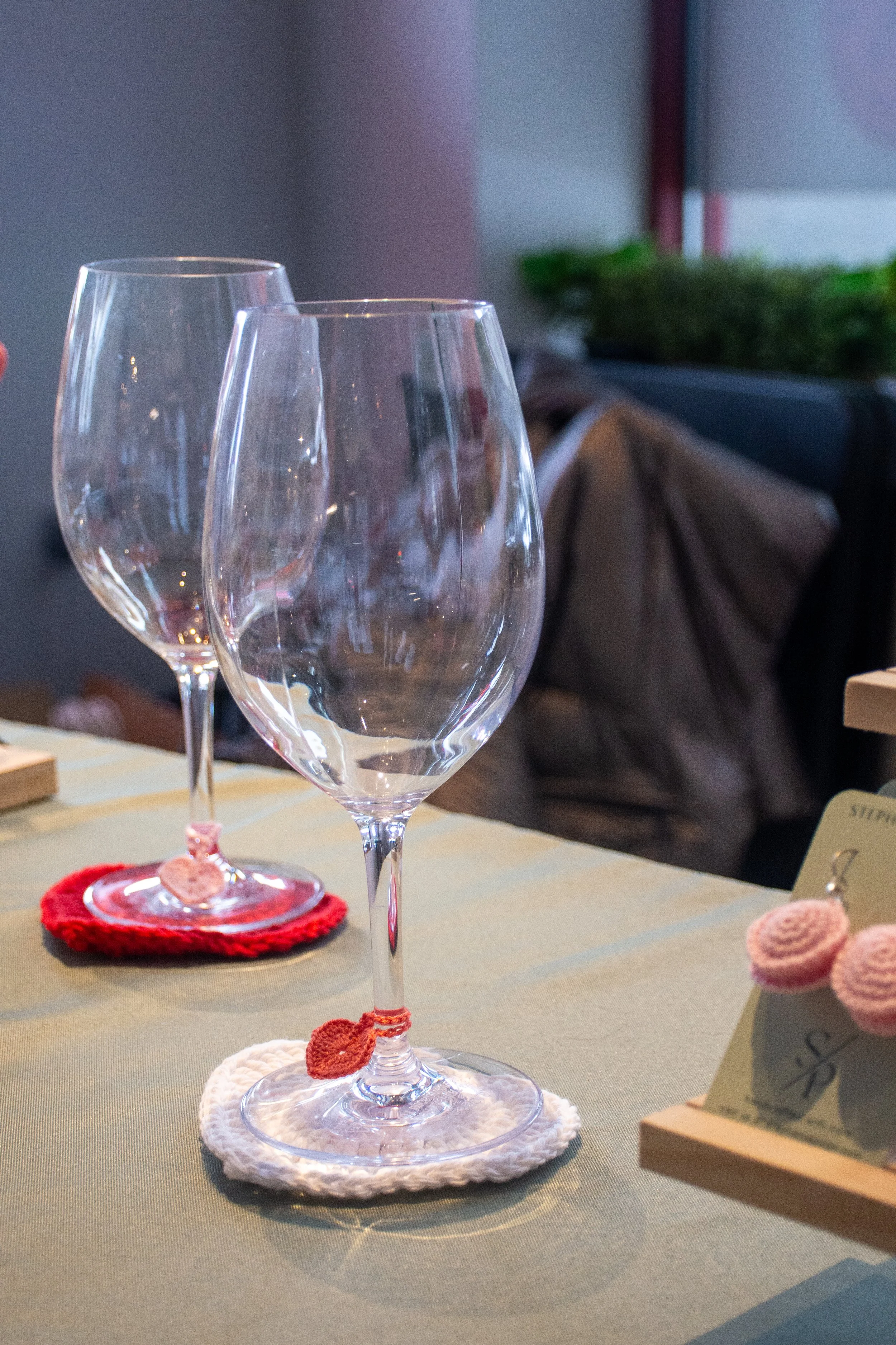 Two empty wine glasses on a table with crocheted coasters, one white and one pink, in a cozy indoor setting.