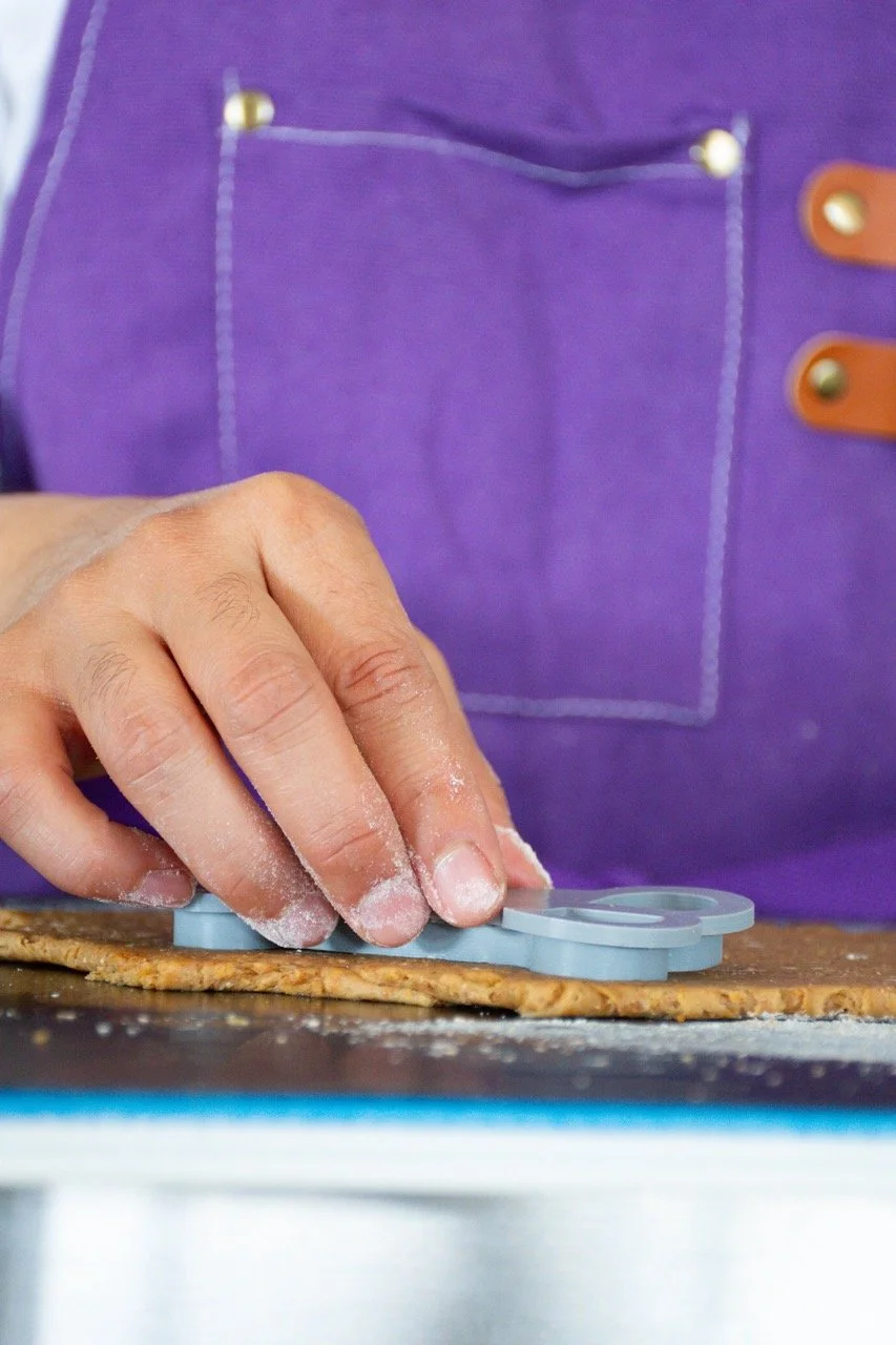 Close-up of a person's hand using a cookie cutter on dough, with a purple apron in the background.