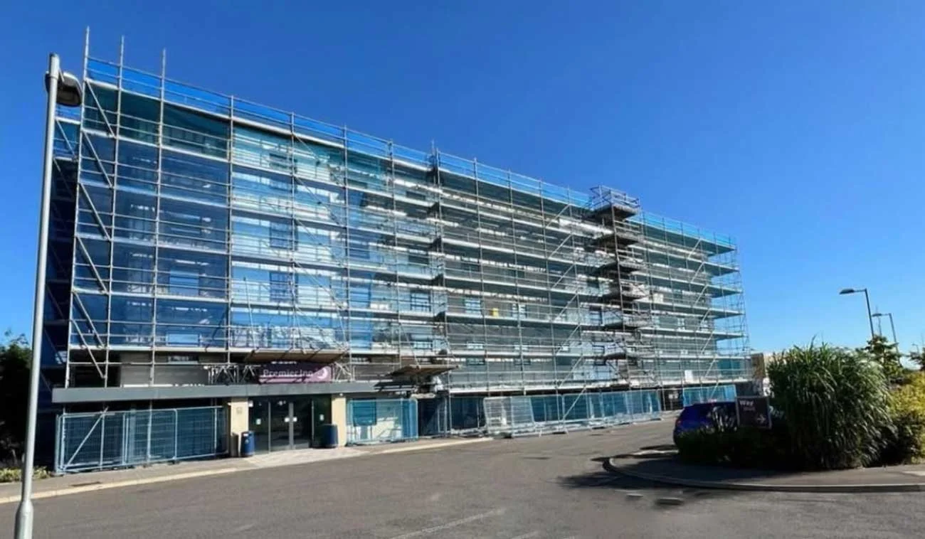 A multi-story office building under construction with scaffolding and temporary protective barriers.