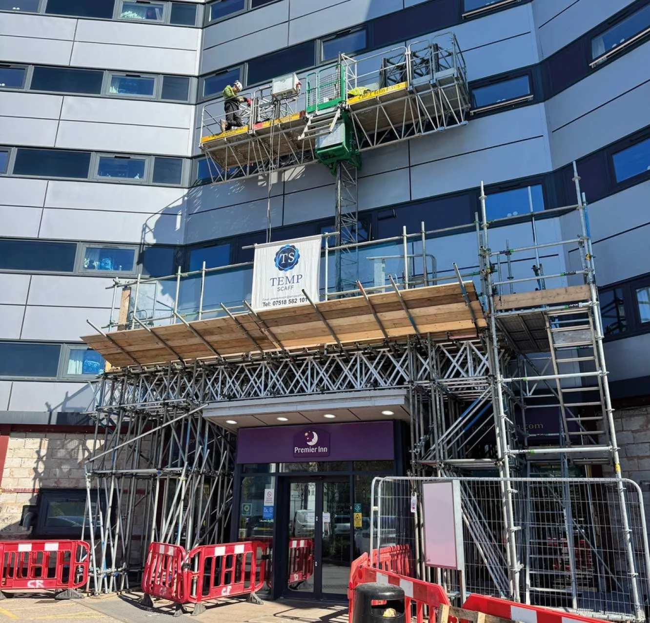 Construction workers on scaffolding at the entrance of a building with a sign reading 'Premier Inn'.