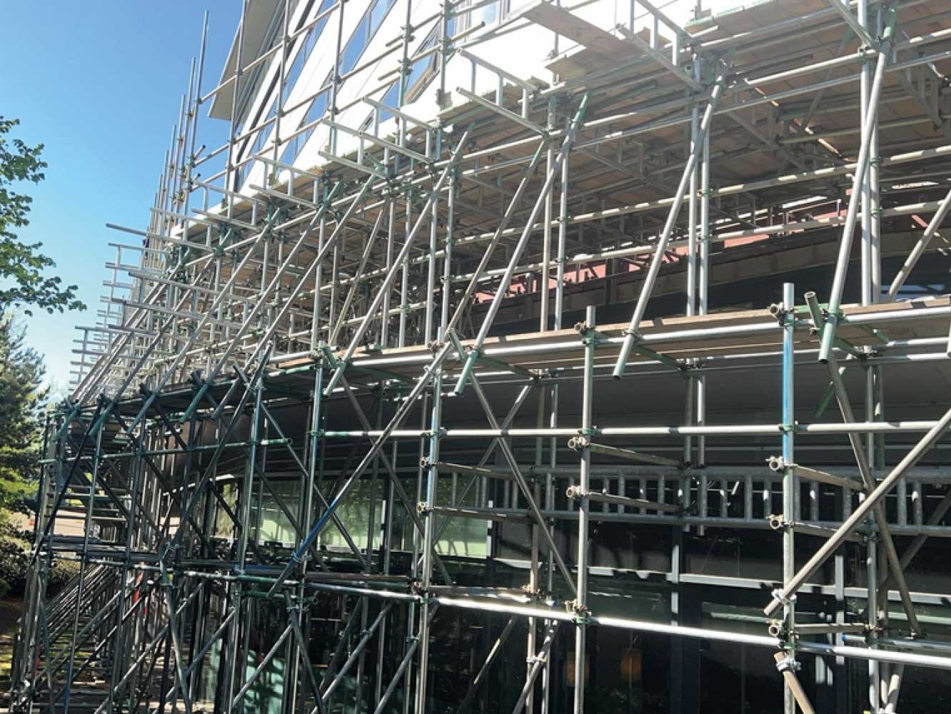 Construction scaffolding surrounding a modern building with glass windows, under a clear blue sky.
