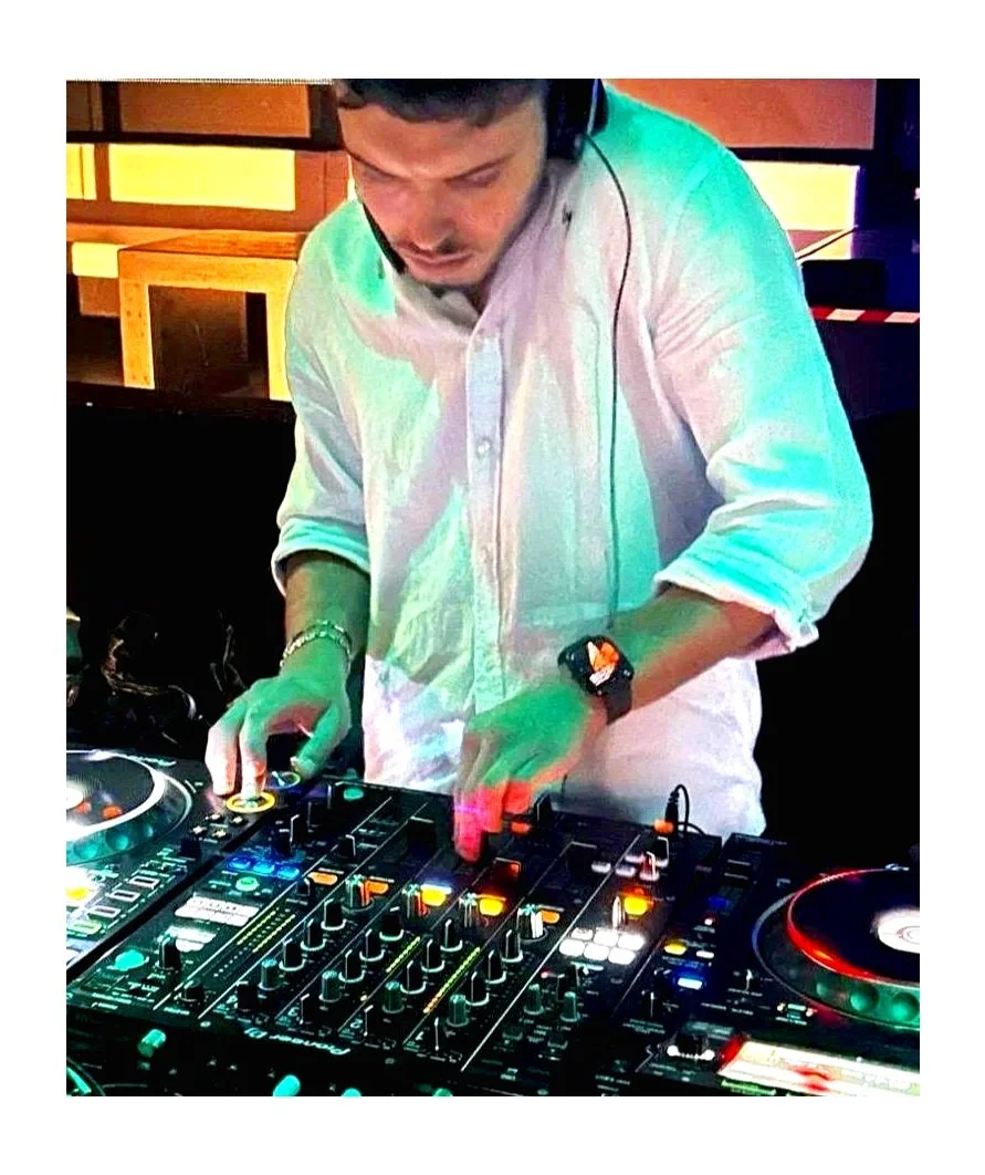 DJ che mixa musica con un controller DJ, indossa un orologio e cuffie, in un ambiente con luci colorate.