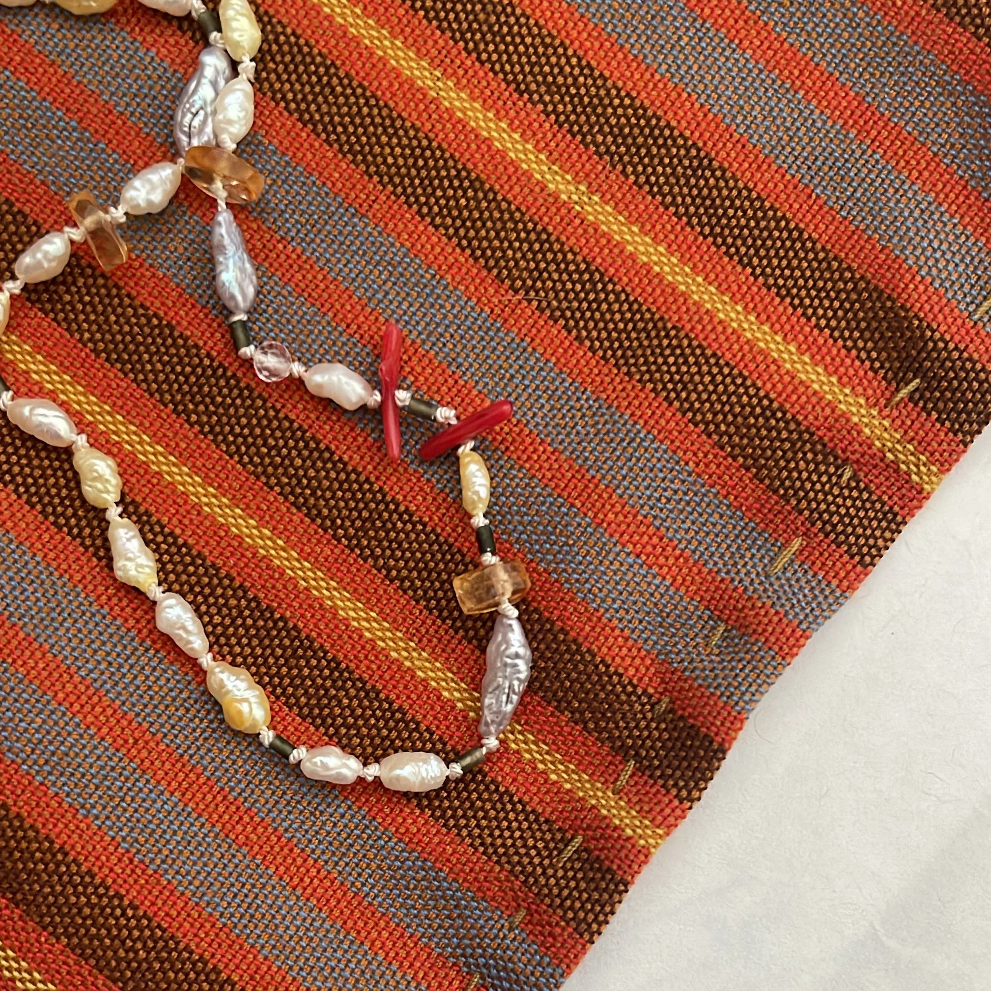 Close-up of a beaded necklace with white, brown, and black beads lying on a woven, multicolored, striped fabric.