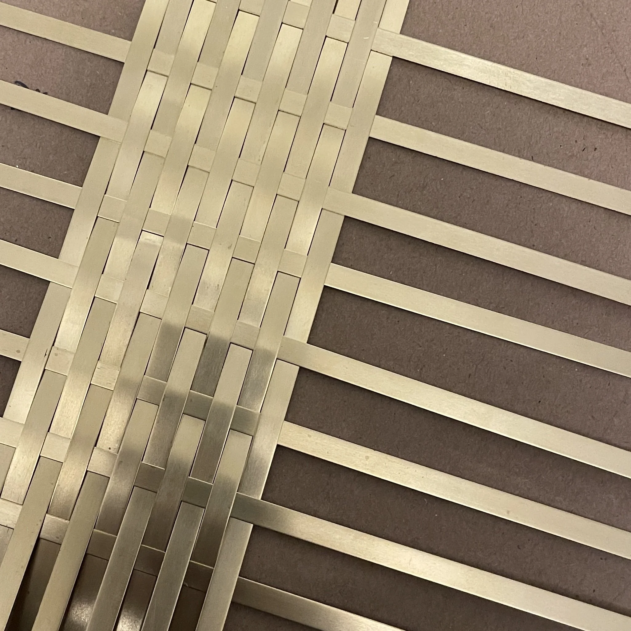 An unfinished group of brass strips woven as a surface.