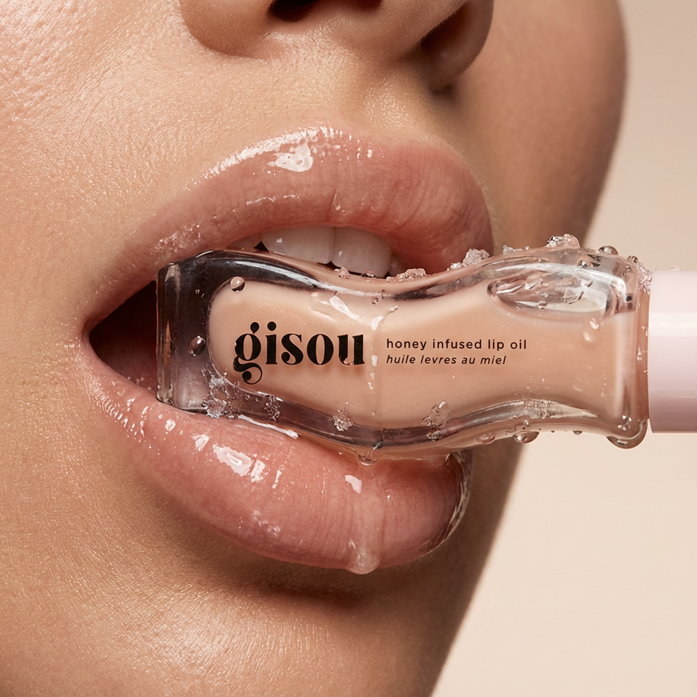 Close-up van lippen met een doorzichtige fles Gisou Honey Infused Lip Oil die gedeeltelijk in de mond zit.