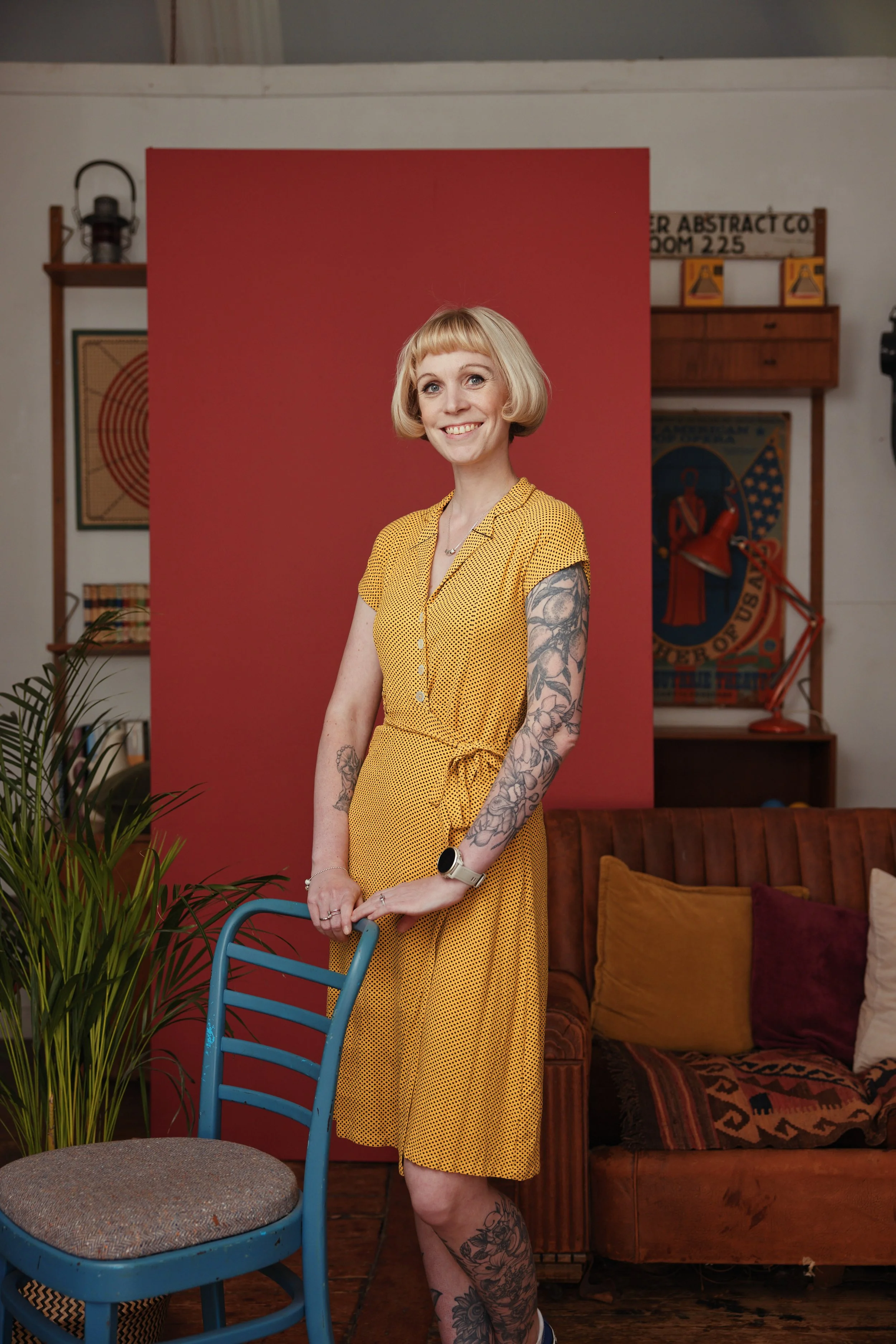 Blonde woman in yellow dress standing next to blue chair
