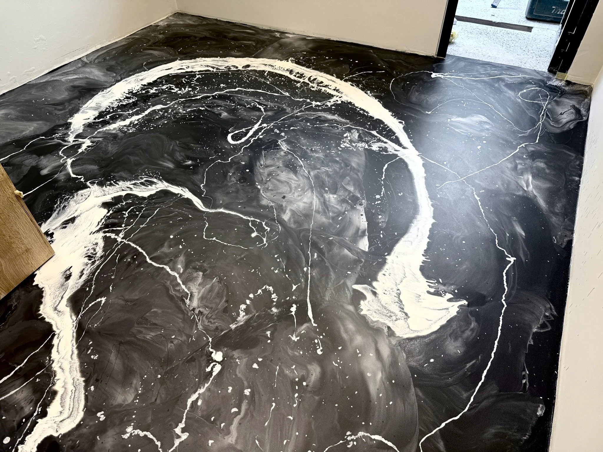 Close-up of a black and white marbled epoxy resin floor with swirling patterns and white veining in a room near the doorway.