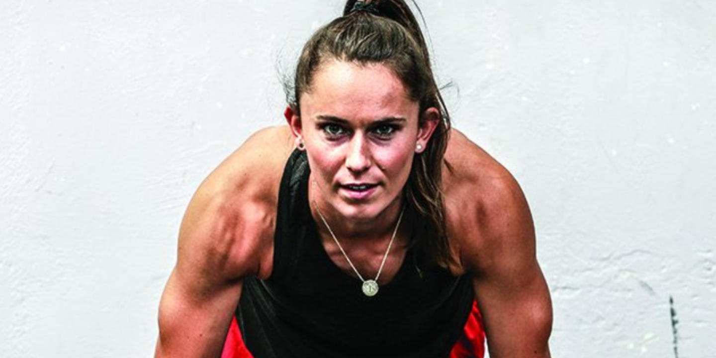 Young woman in workout attire, doing a push-up, looking focused.