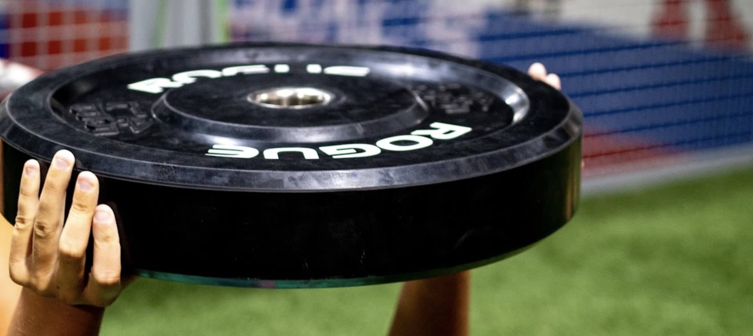 holding a black weight plate overhead during a workout or sports activity