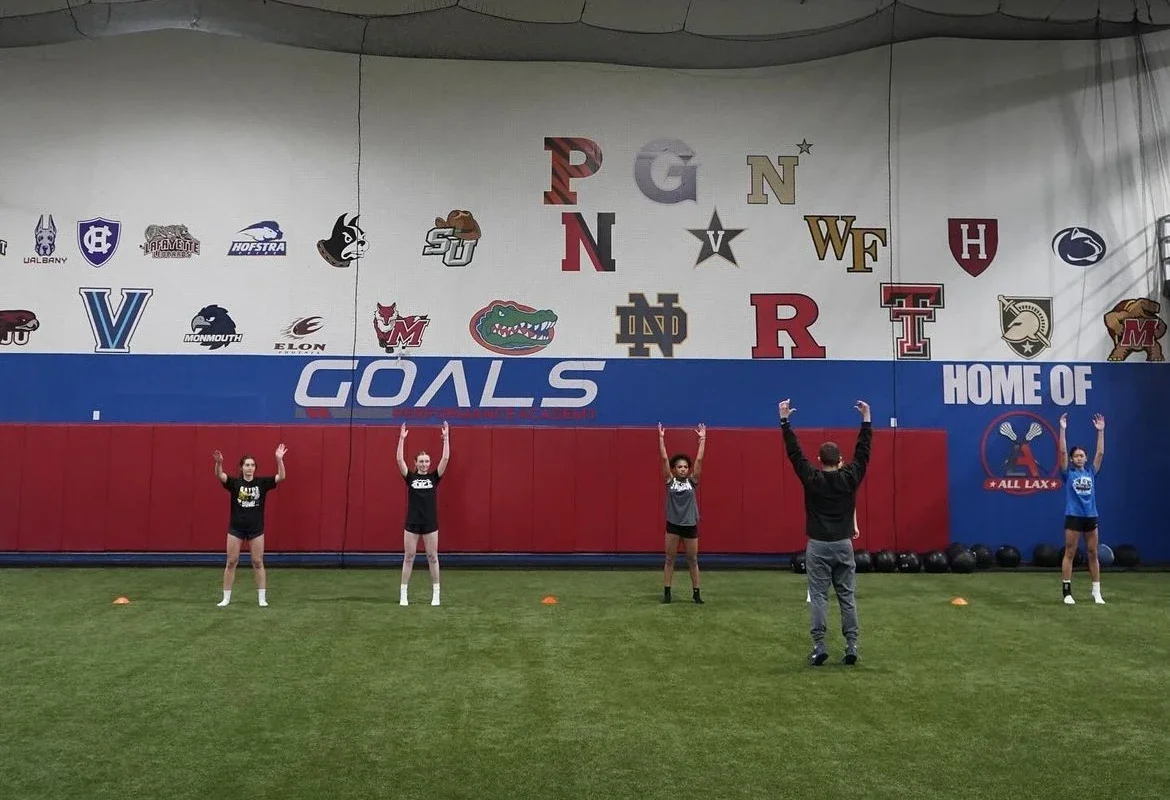 Jump series training practicing drills in an indoor sports facility with logos of college teams on the wall.