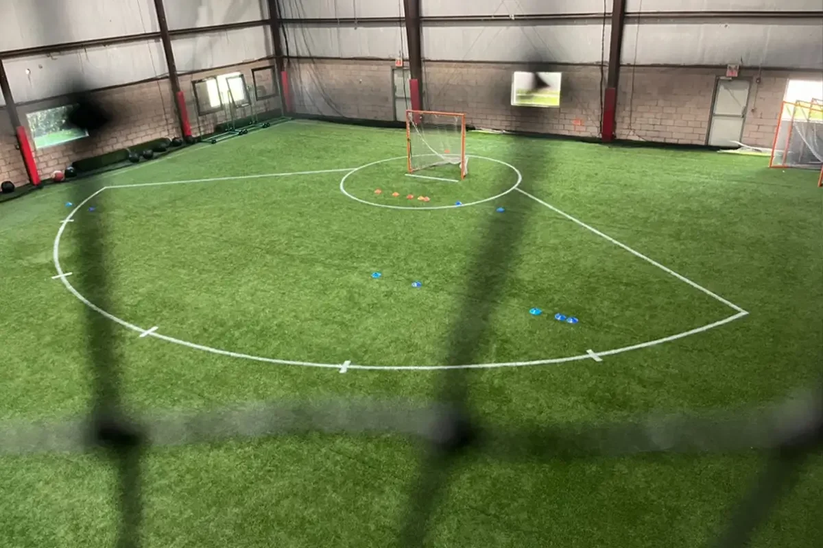 Indoor sports facility with a turf space, involving a goal and cones for drills. The field has white lines marking the boundaries.