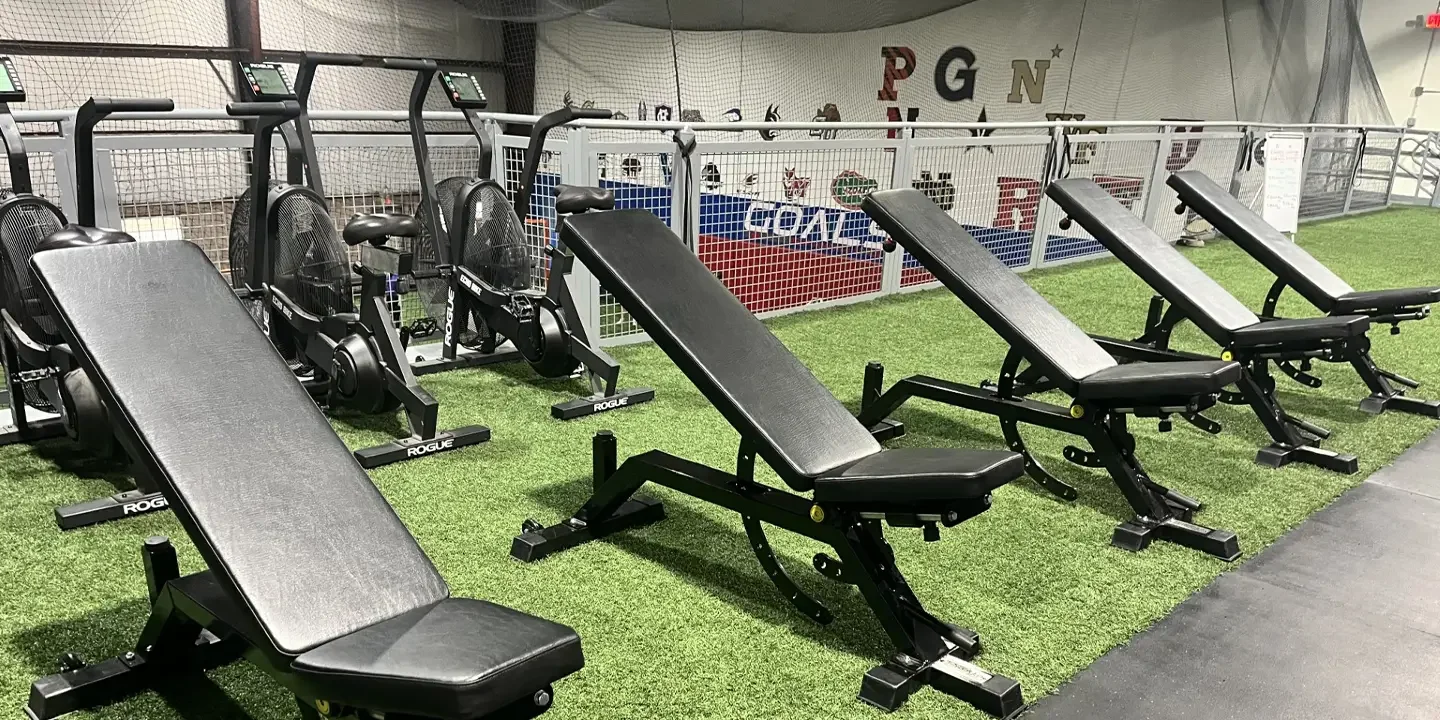 Indoor gym area with adjustable workout benches and rowing machines placed on artificial green turf.