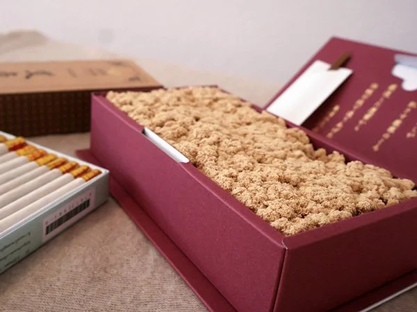 Verschiedene Zigarettenstummel und eine große rosa Schachtel mit Tabak auf einem Tisch.