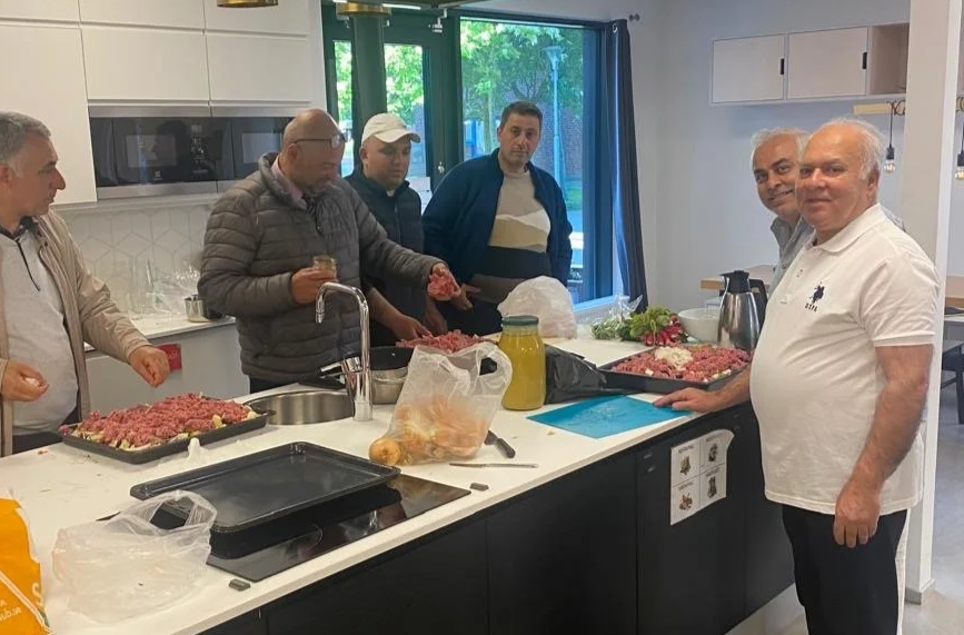 Group of men preparing meat at a kitchen counter in a modern, well-lit kitchen with large windows.