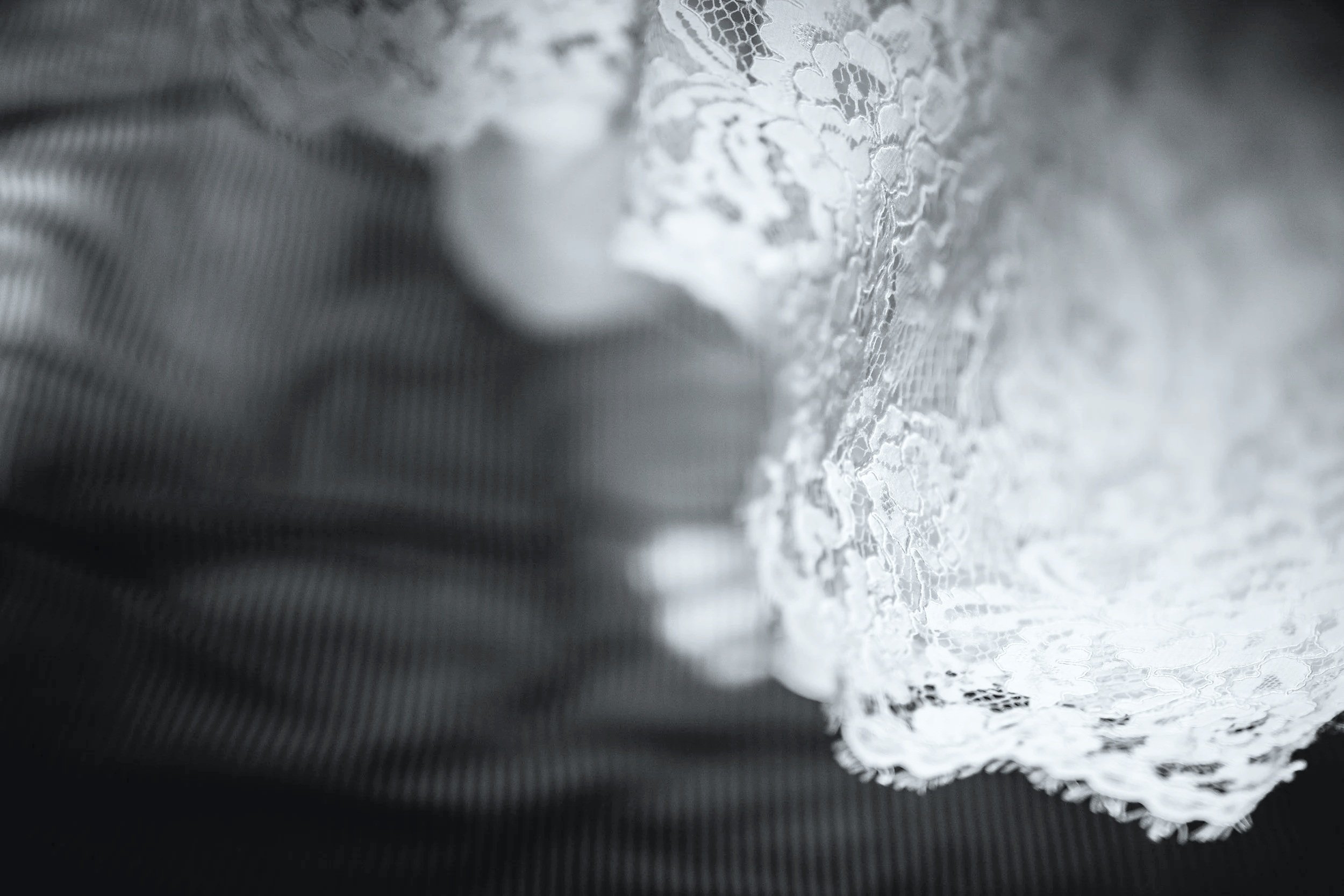 Close-up image of lace fabric, showing intricate floral patterns, against a dark blurred background.