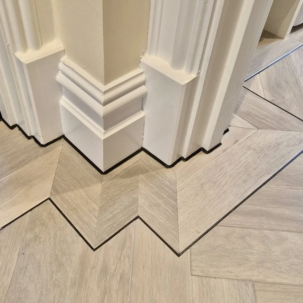 Black floorline mastic work. Close-up of a corner molding with black contrasting floorline detailing on a light wood floor.