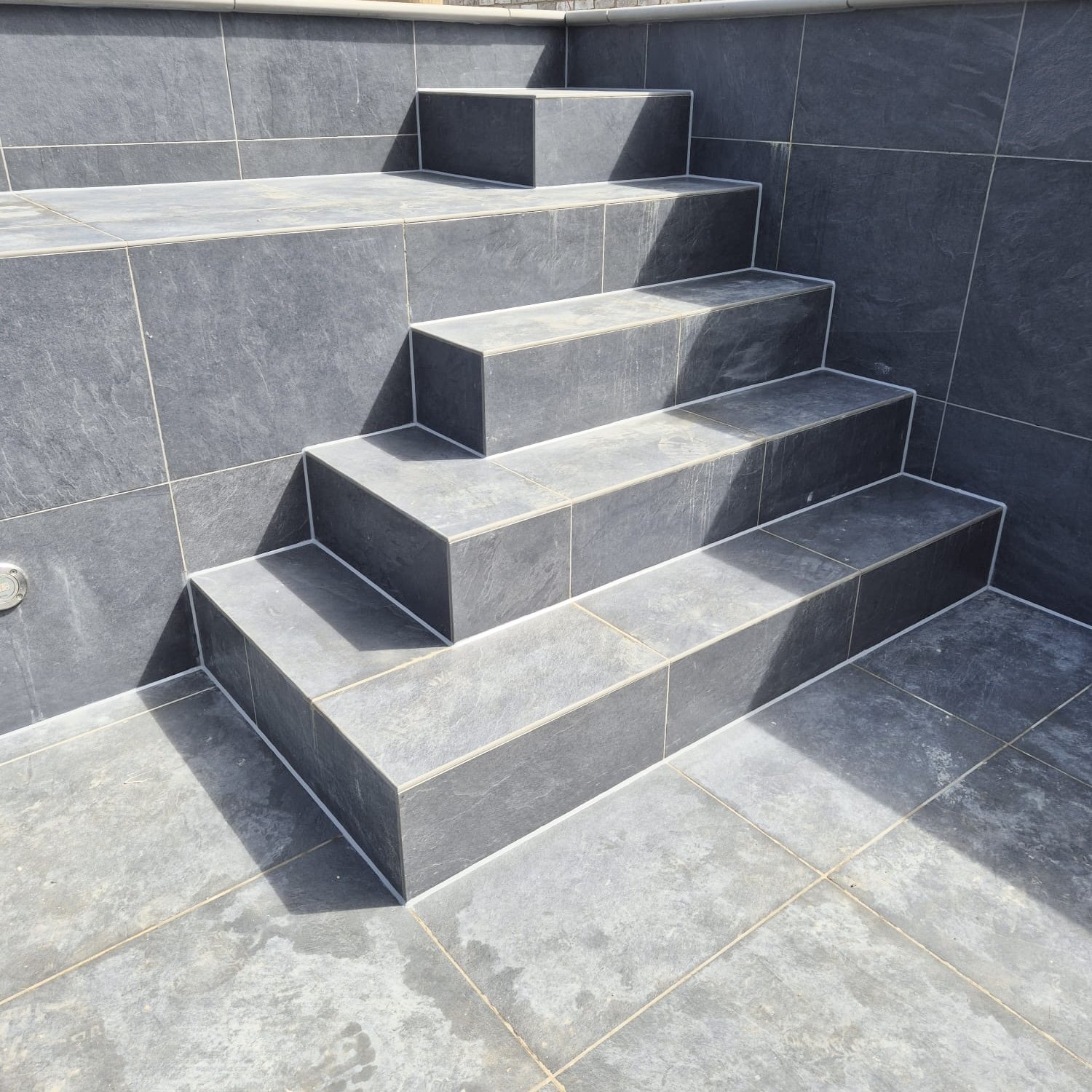 Slab Work Mastic. Gray tiled outdoor staircase with a small landing and three steps leading up.
