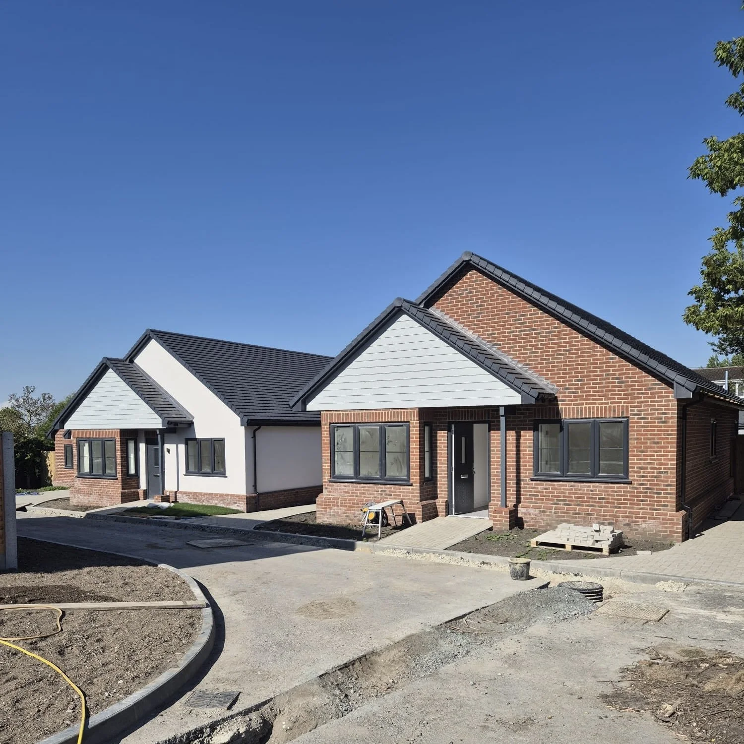 Newly constructed single-family houses with brick and white siding, black windows mastic, and blue sky. Construction materials and tools visible in front.