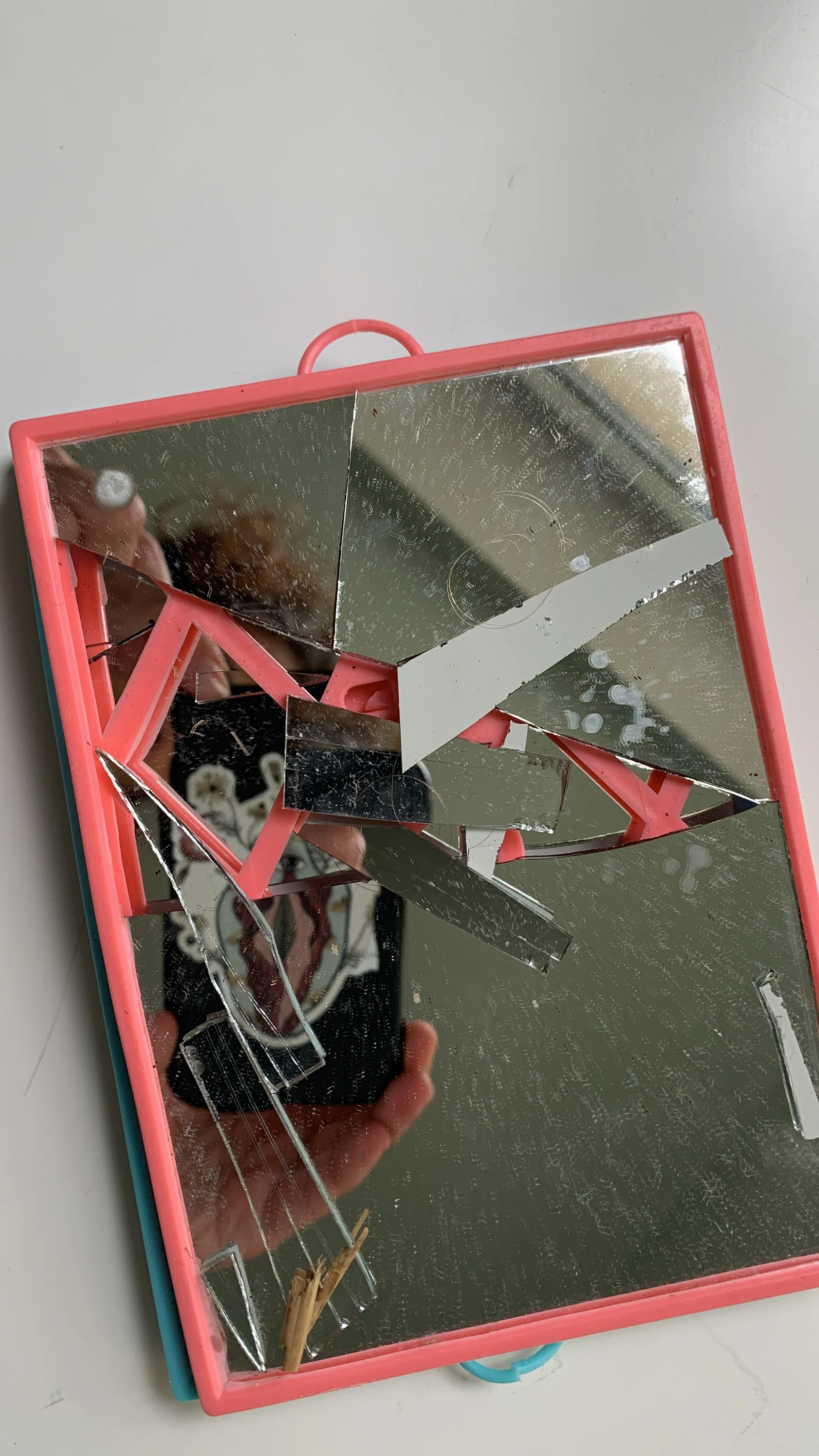 Broken pink-framed mirror with several shattered glass pieces and scratches on the surface.